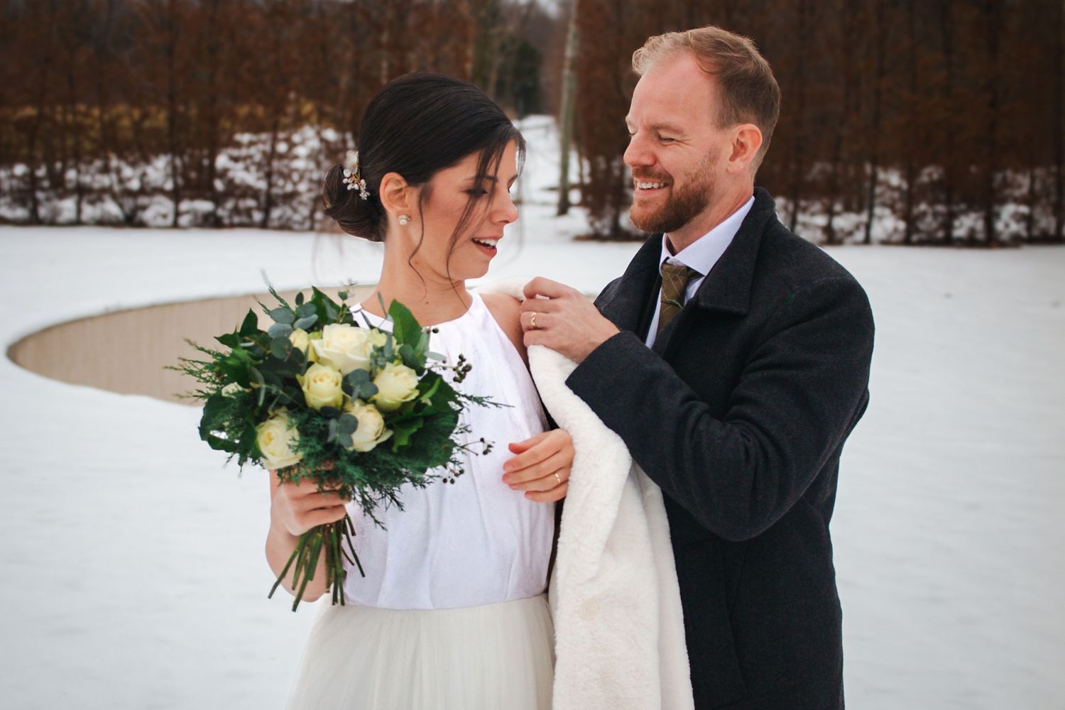 A joyful wedding couple shares an intimate moment in a snowy winter setting.