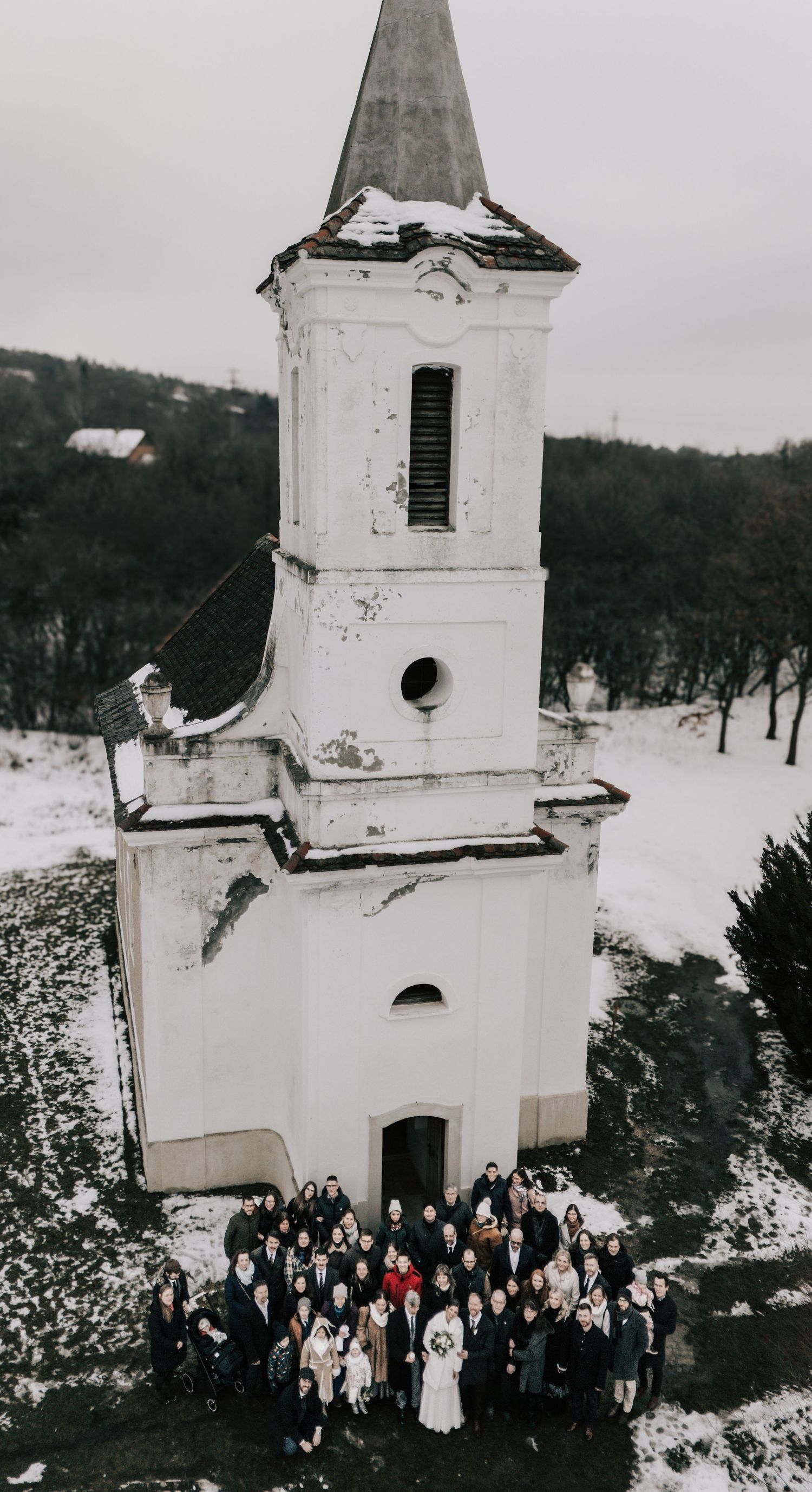 Winter wedding group photo outside a white church in snowy landscape.