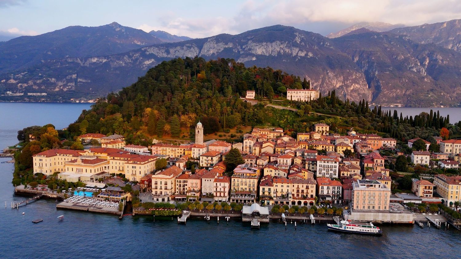 Panoramic view of Lake Como in Italy with mountains, waterfront villas, and traditional Mediterranean architecture.
