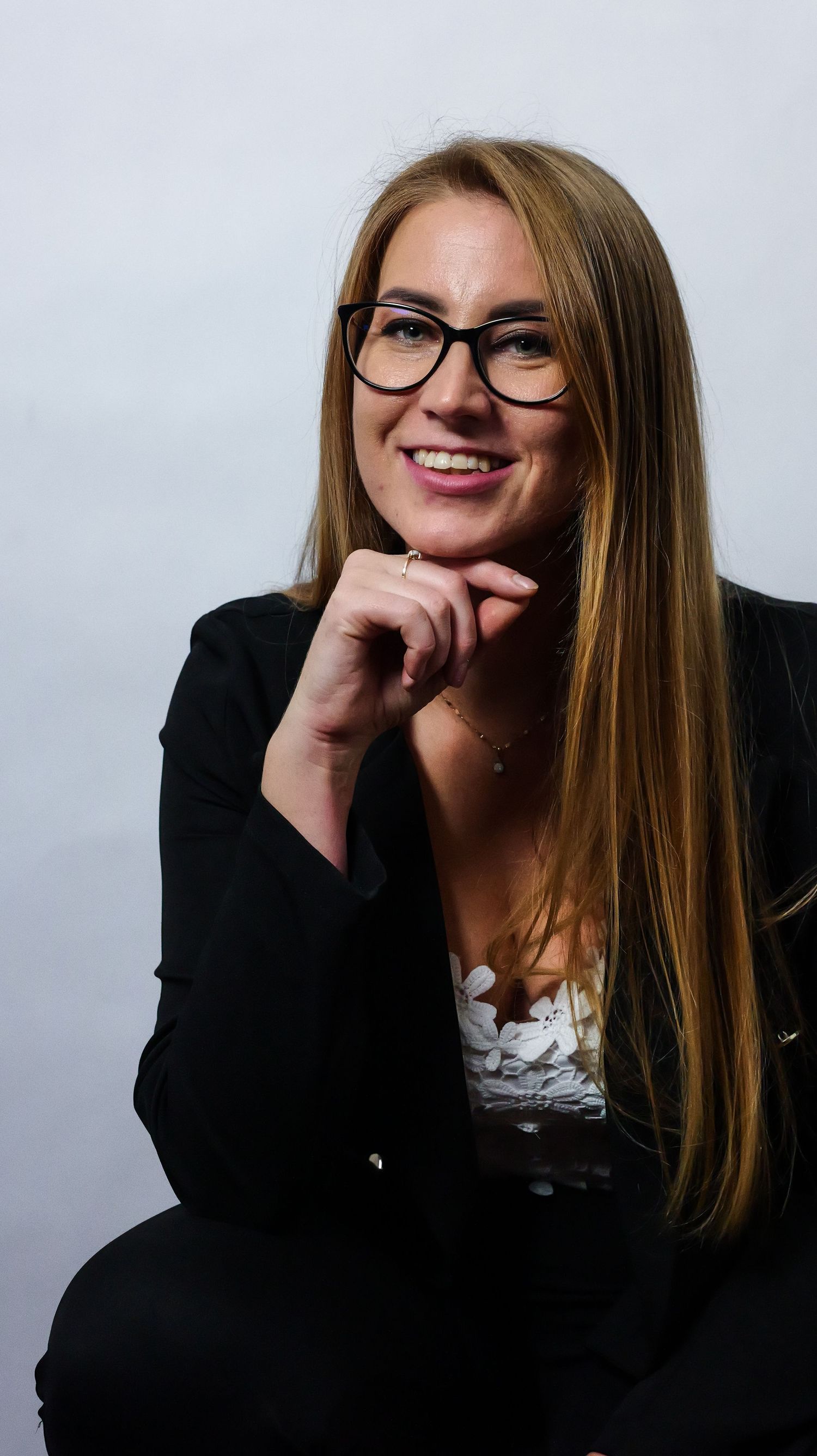 Professional portrait of a person in black blazer and glasses against white background.