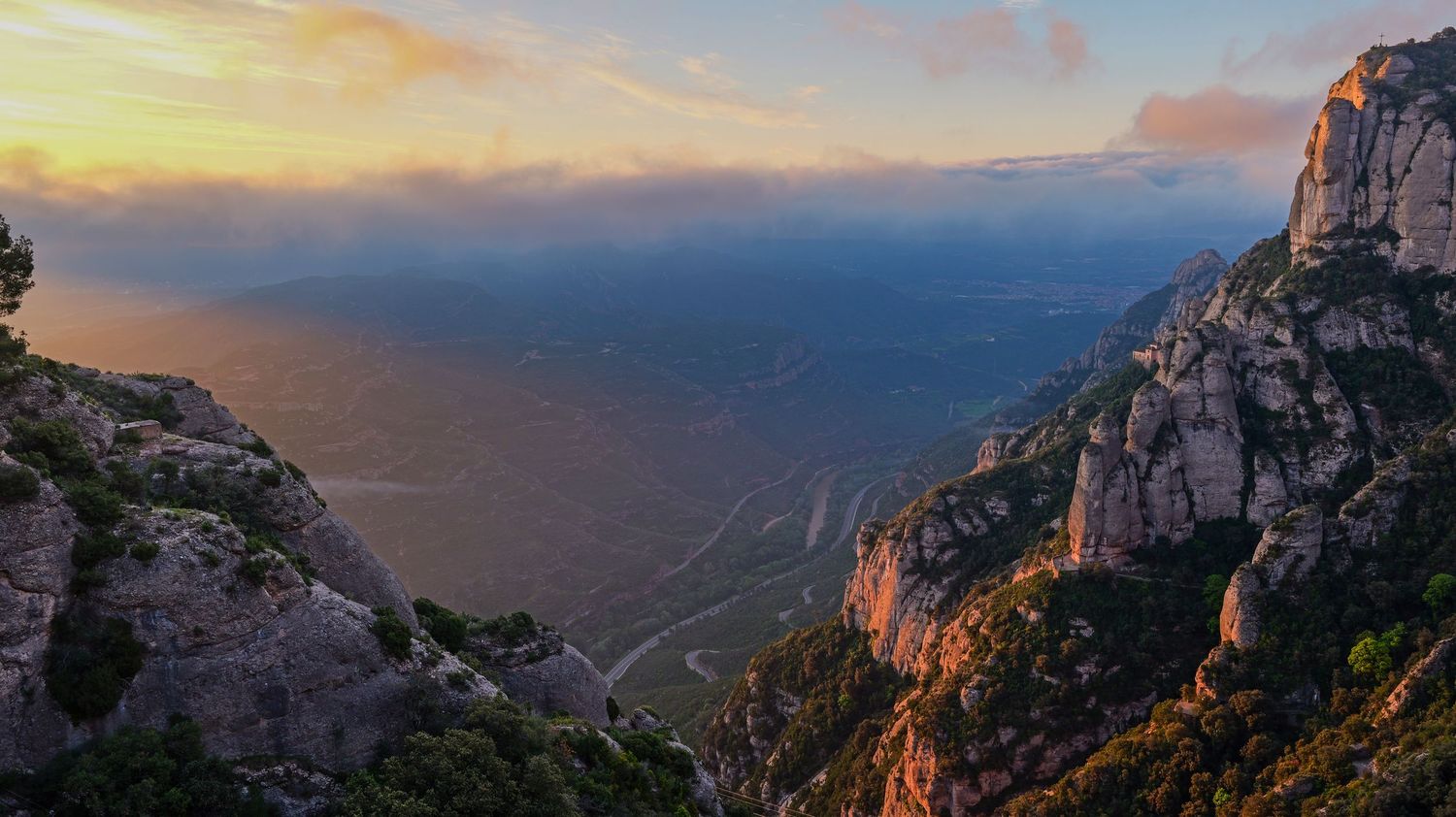 Panoramic mountain landscape with dramatic sunset sky and rocky cliffs overlooking a vast valley.