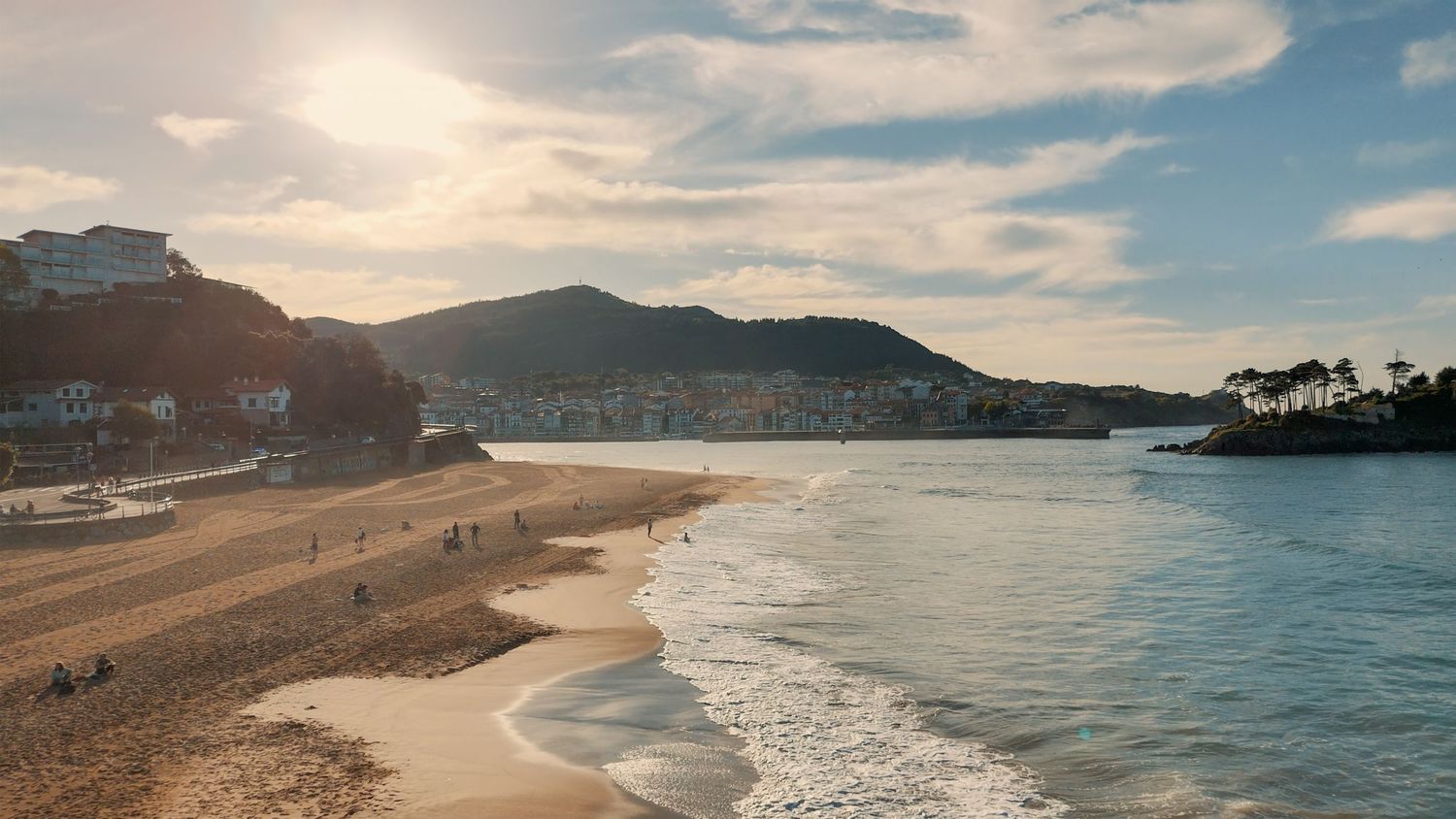 Panoramic coastal landscape with sandy beach, blue sky and mountains in the distance at sunset.