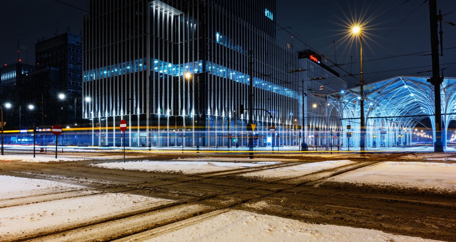 Snow-covered train tracks illuminated by bright station lights create a serene winter nighttime scene at a railway platform.