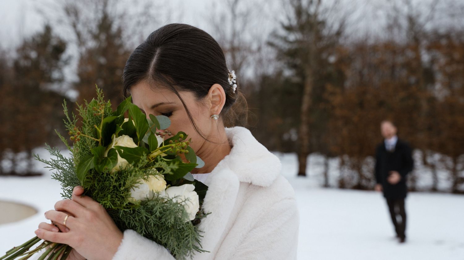 A snowy winter scene with evergreen branches in the foreground and figures walking in the background.
