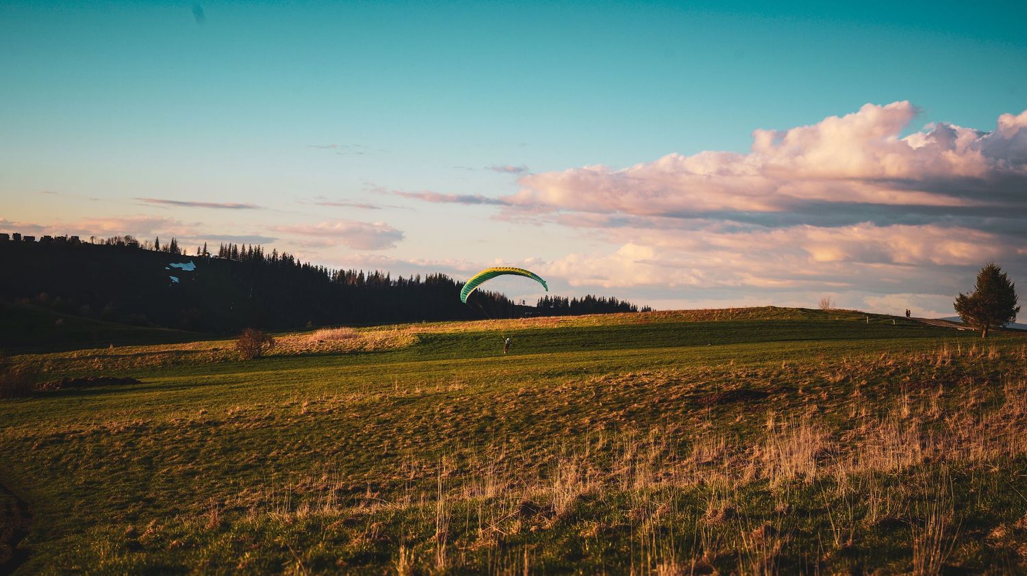 A panoramic view of rolling hills and farmland under a dramatic sunset sky with scattered clouds.