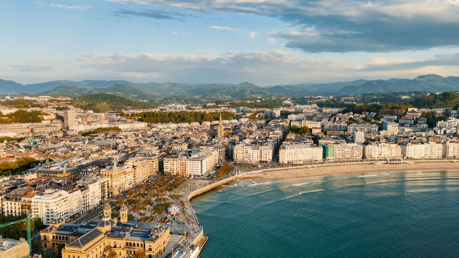 Panoramic aerial view of a coastal San Sebastian city with mountains, beaches, and blue waters stretching along the shoreline.
