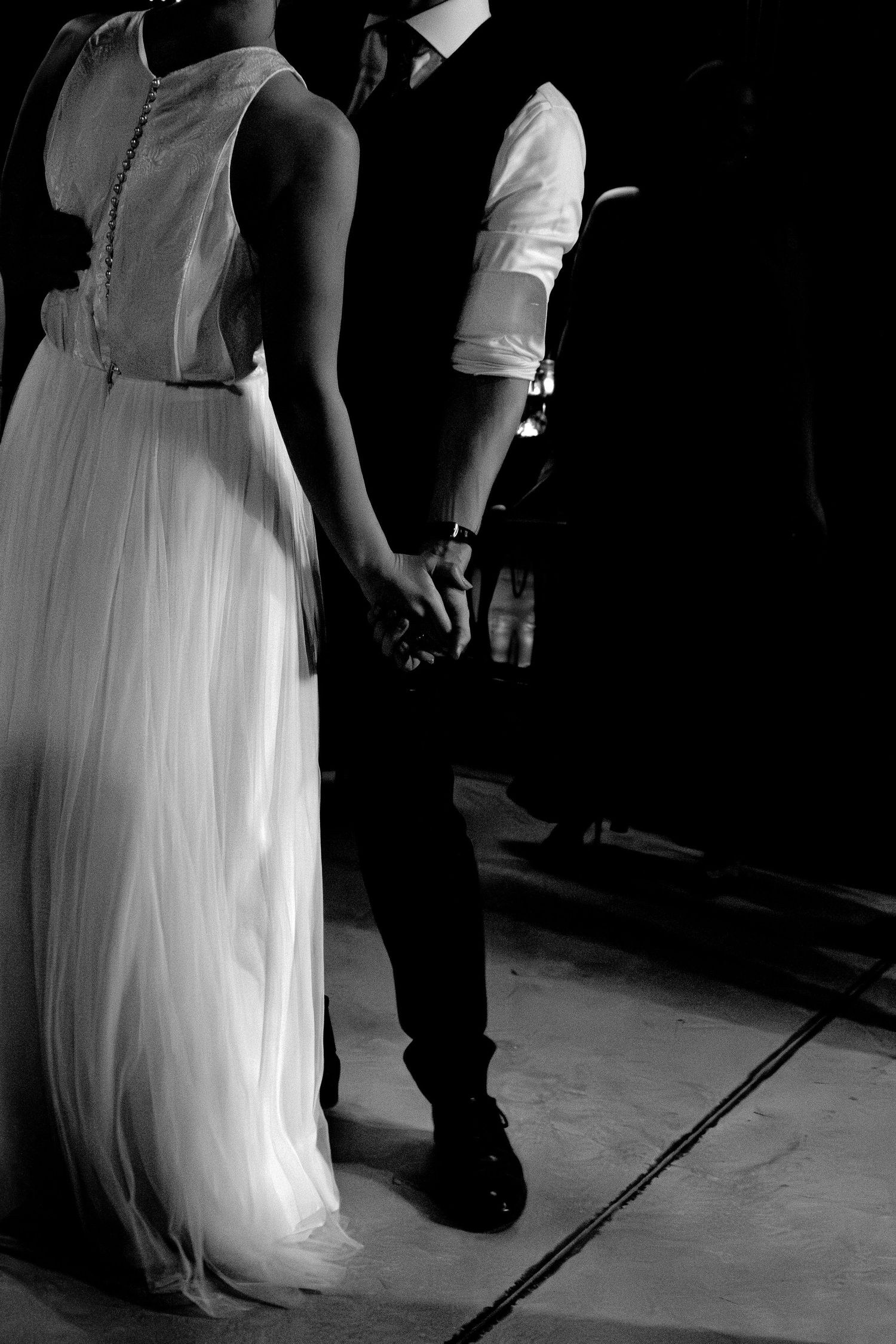 Black and white photo of dancing feet at a wedding, showing a white dress and dark suit.