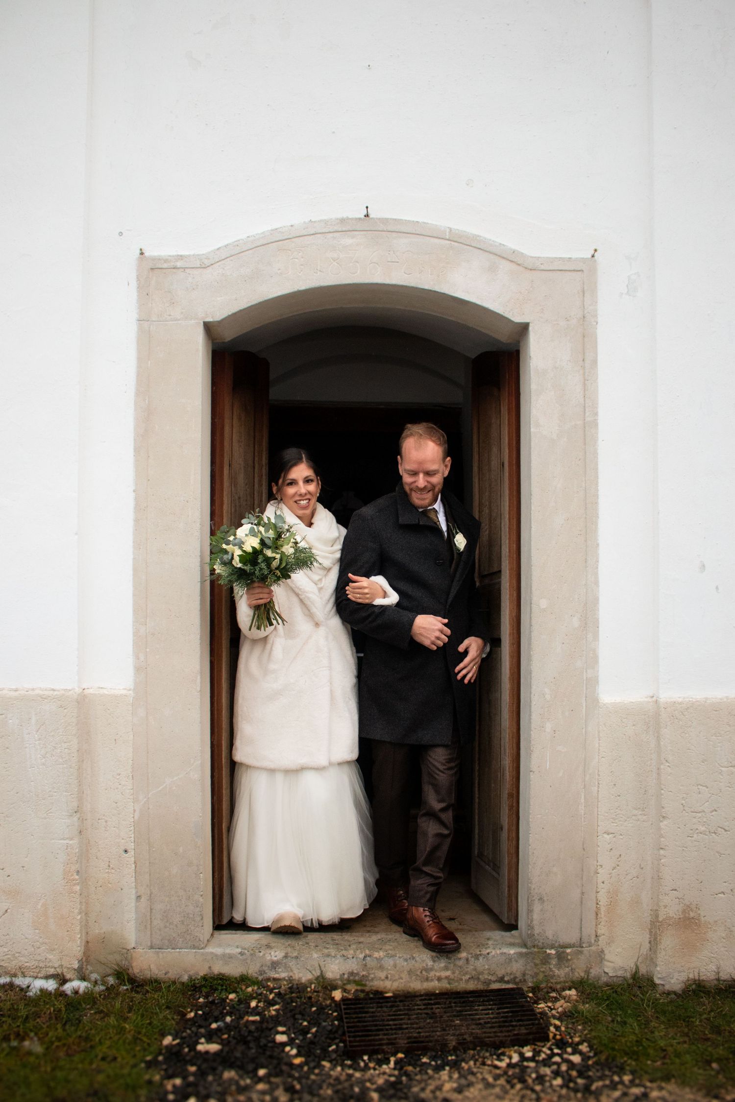 A couple emerges through a white church doorway during their winter wedding ceremony.