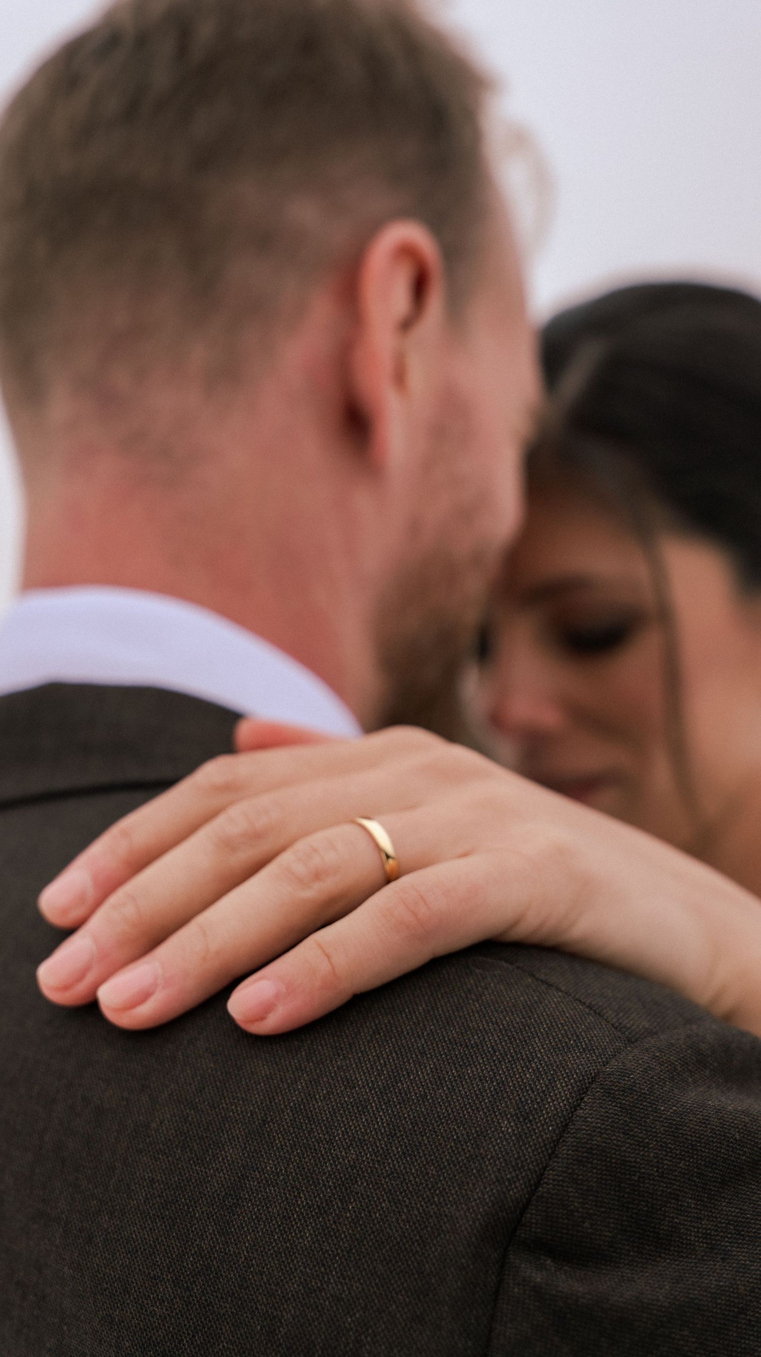 A delicate hand with a wedding ring rests on a dark suit jacket.
