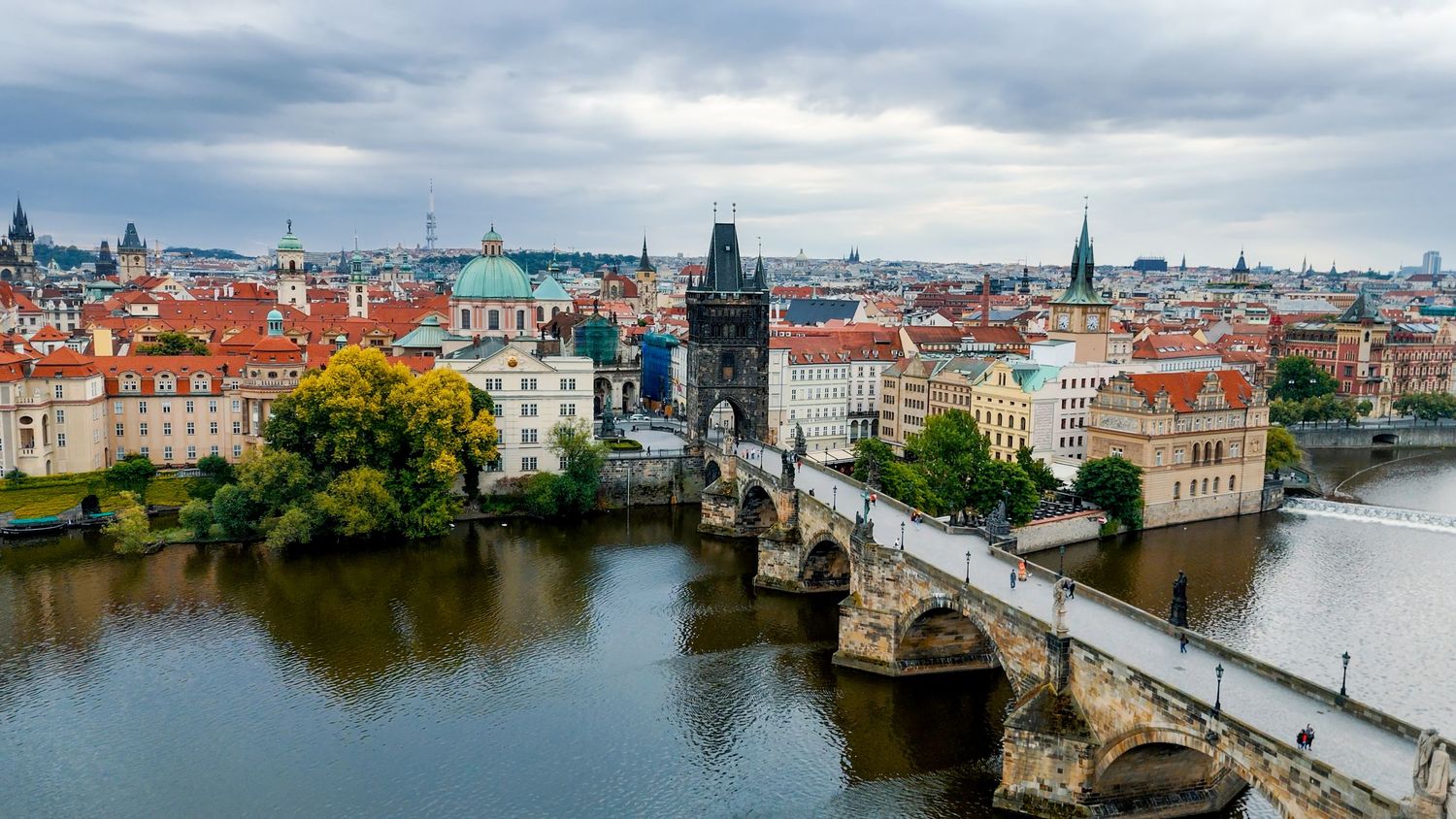 Panoramic cityscape view of Prague showing historic architecture and bridges over the Vltava River.