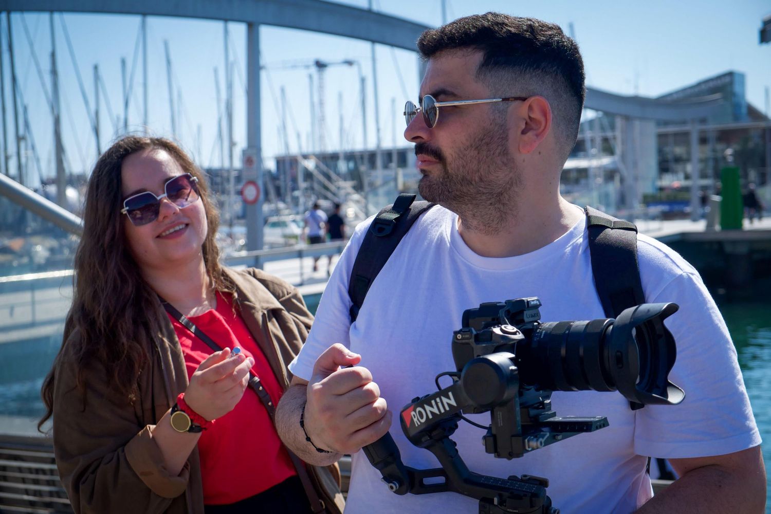 Couple enjoying a sunny day at a marina with boats in the background.