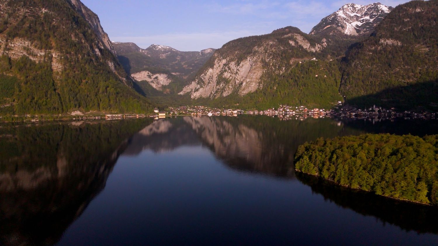 Scenic view of Hallstatt Lake in Austria with mountains reflected in calm waters during sunset.