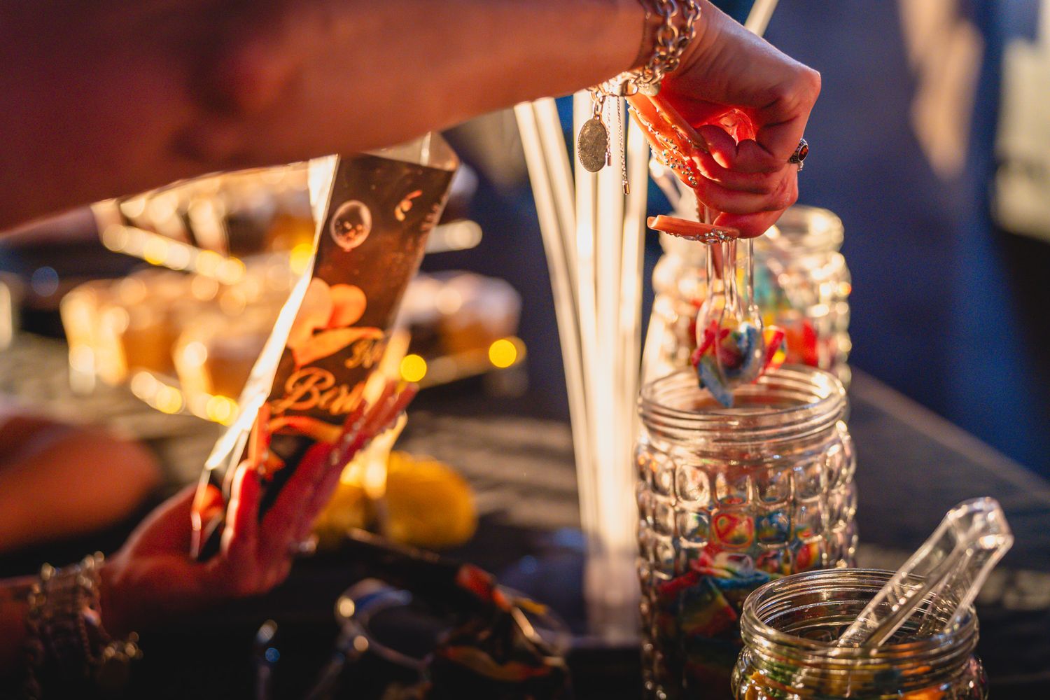 Close-up of a hand picking colorful candy lollipops from a glass jar at a festive candy bar display.