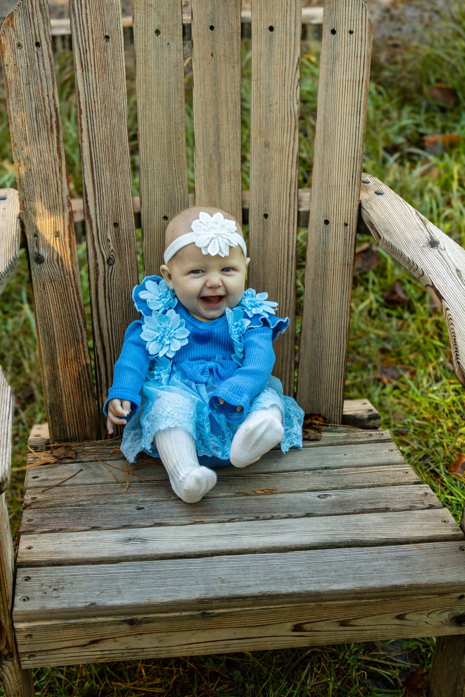 Baby in blue dress sitting on wooden bench during outdoor photoshoot.
