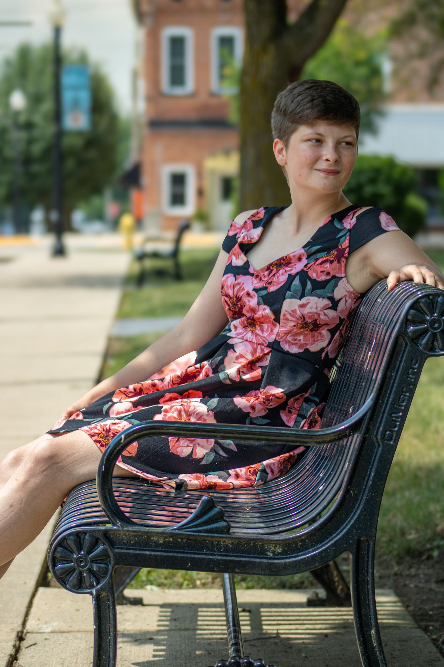 Someone wearing a floral dress relaxes on a black metal park bench in a sunny outdoor setting.