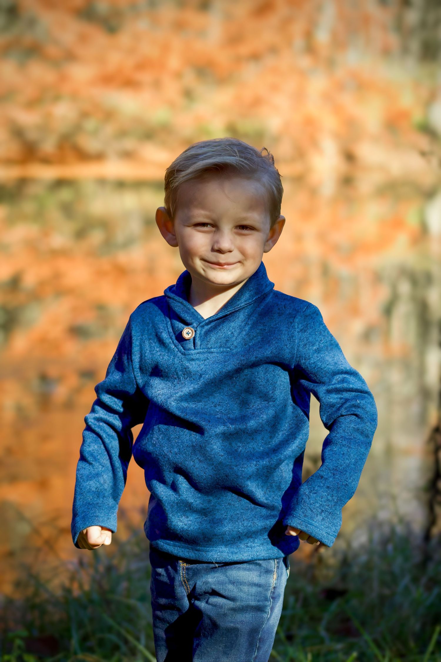 A child wearing a blue sweater and jeans plays outdoors against an orange autumn background.