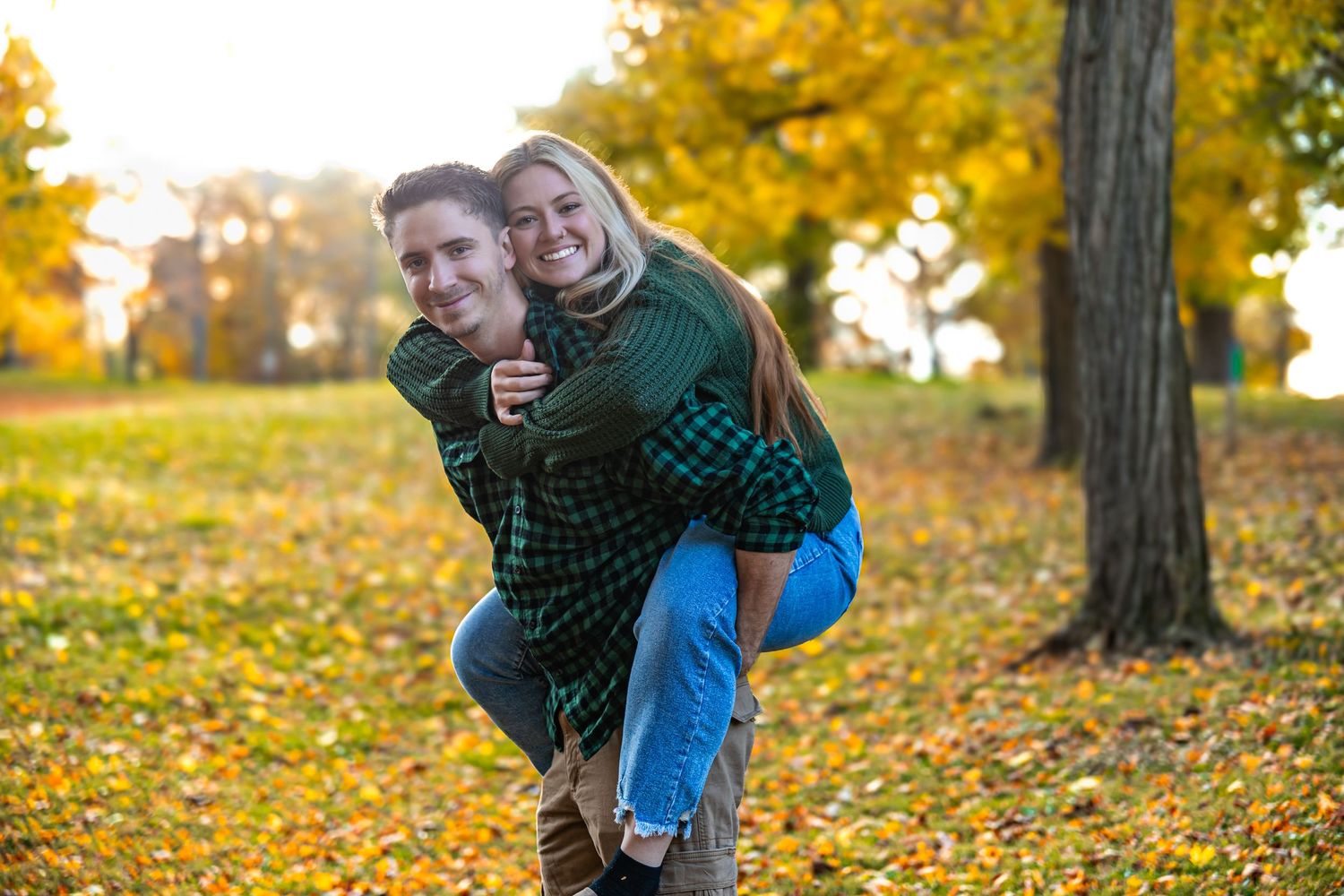 A couple shares a joyful moment together in a vibrant autumn park with golden leaves scattered on the ground.