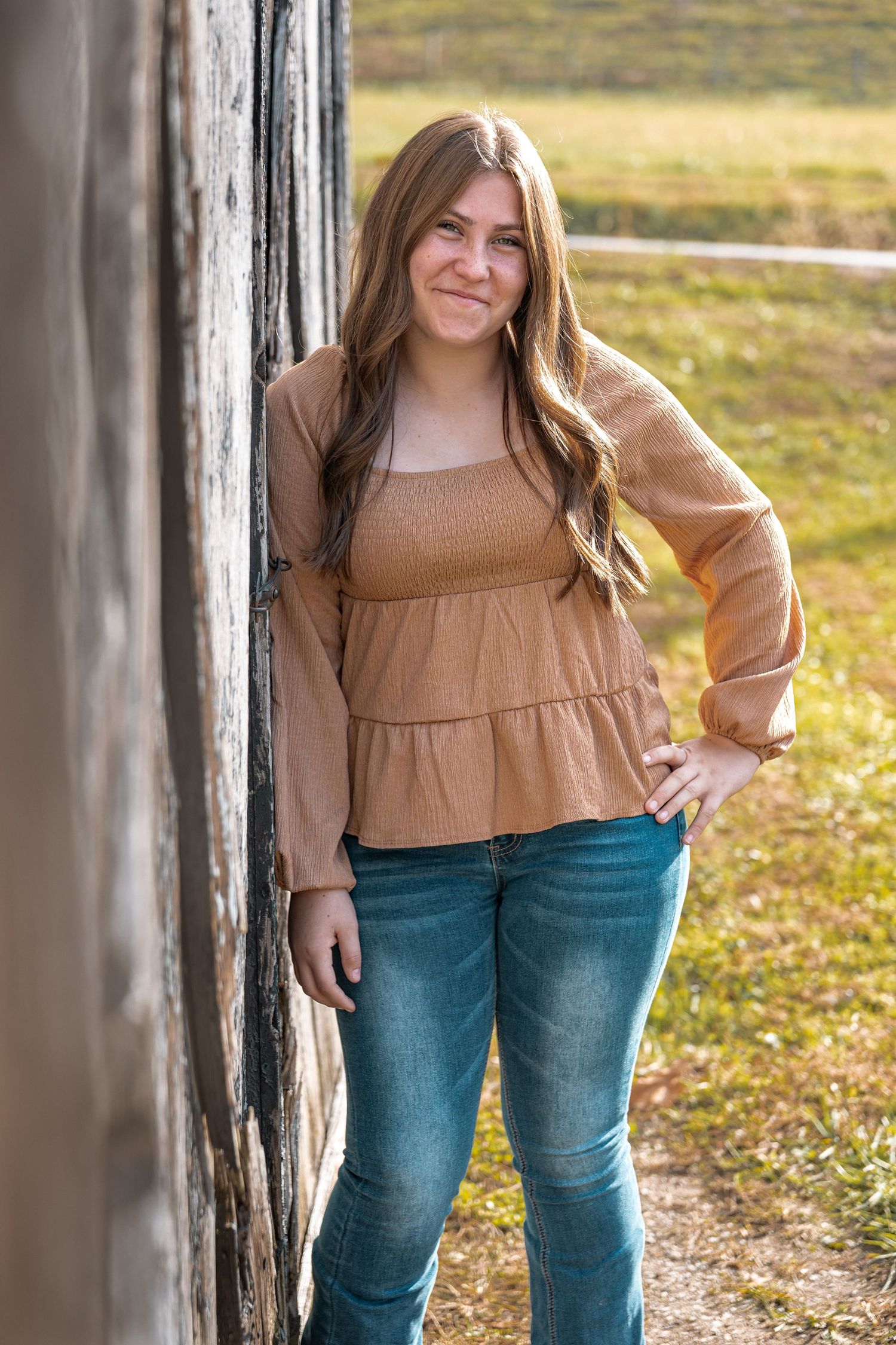 Person in brown top and jeans posing against rustic wooden pillars in golden sunlight.