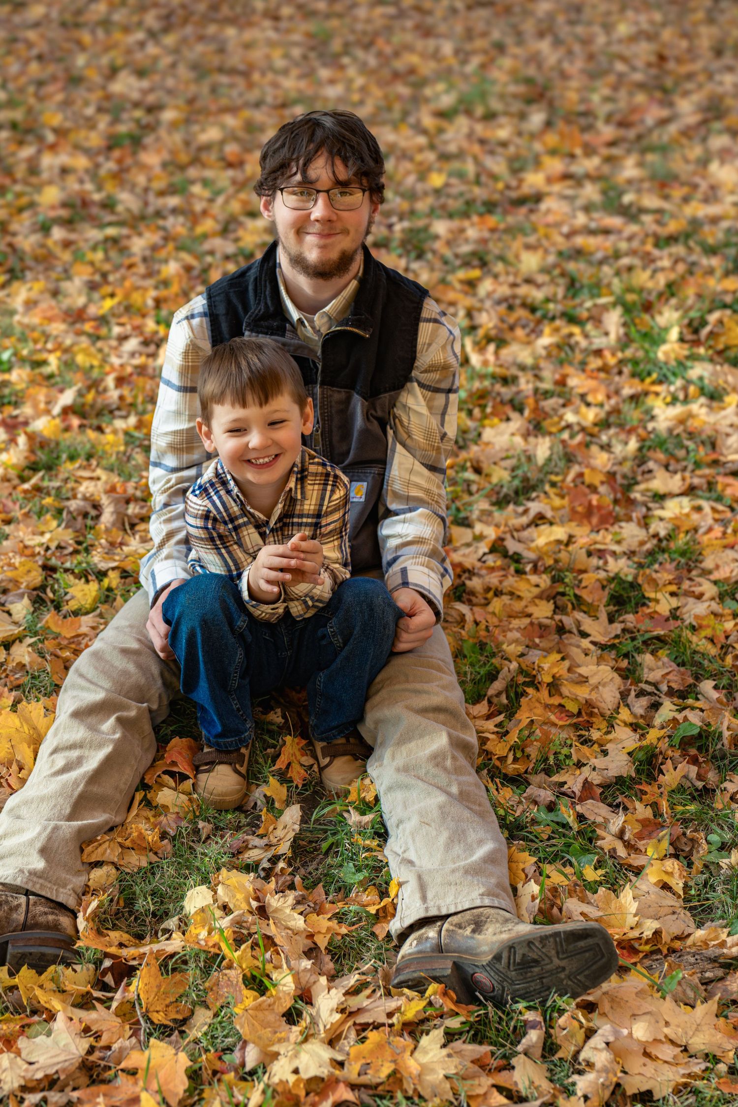 Two people sitting together on fallen autumn leaves in a park on a sunny fall day.
