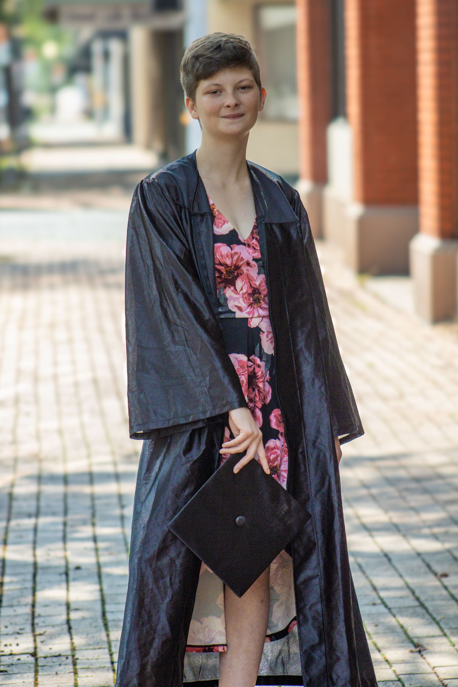 A person in a black robe and floral top poses in a series of four similar photos on a brick walkway.