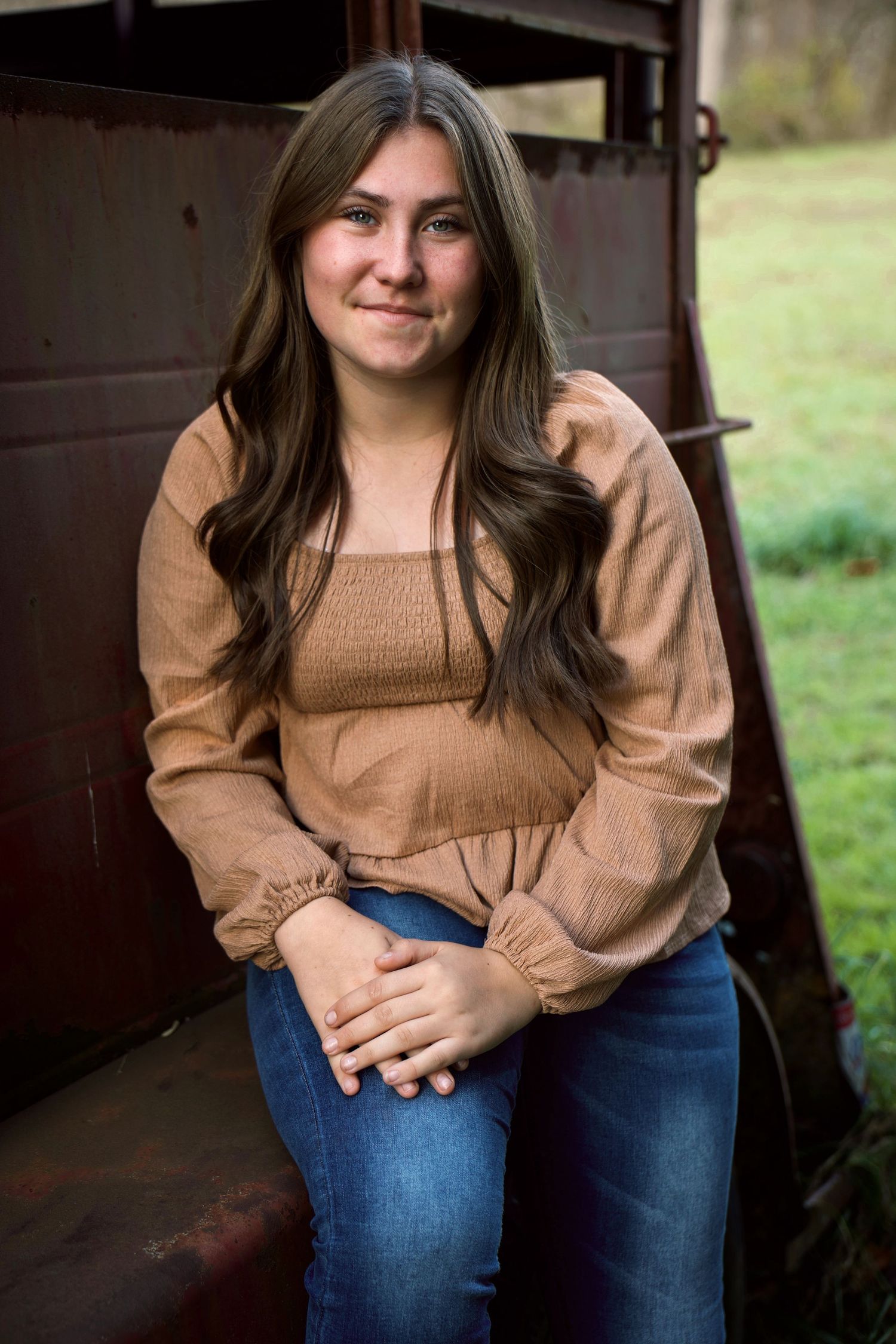 Person wearing brown peasant top and blue jeans poses casually in front of rustic barn setting.