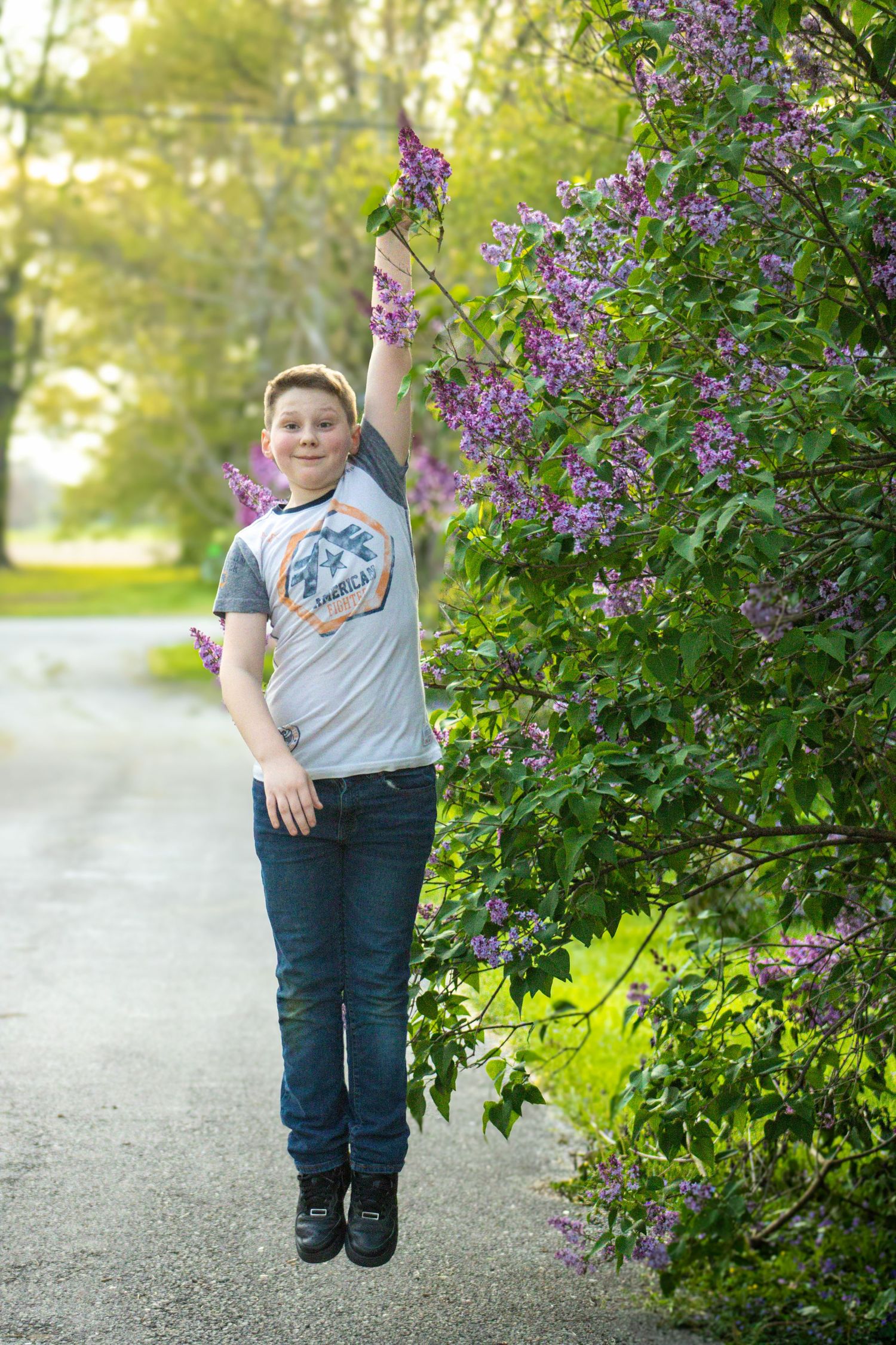 A series of four photos showing a person jumping playfully next to blooming purple lilac bushes on a gravel path.