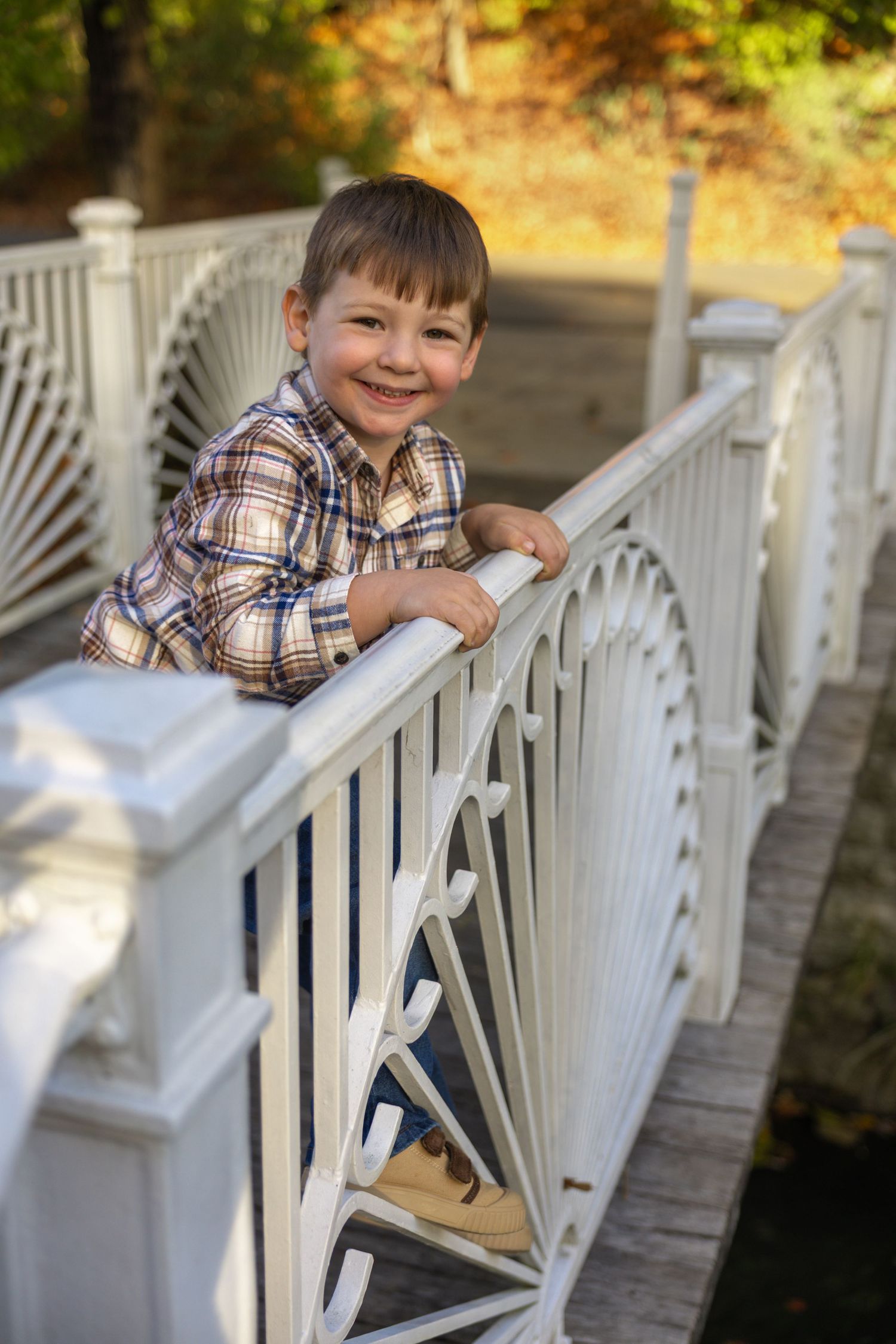 Child posing playfully on white porch railing during autumn photo session.