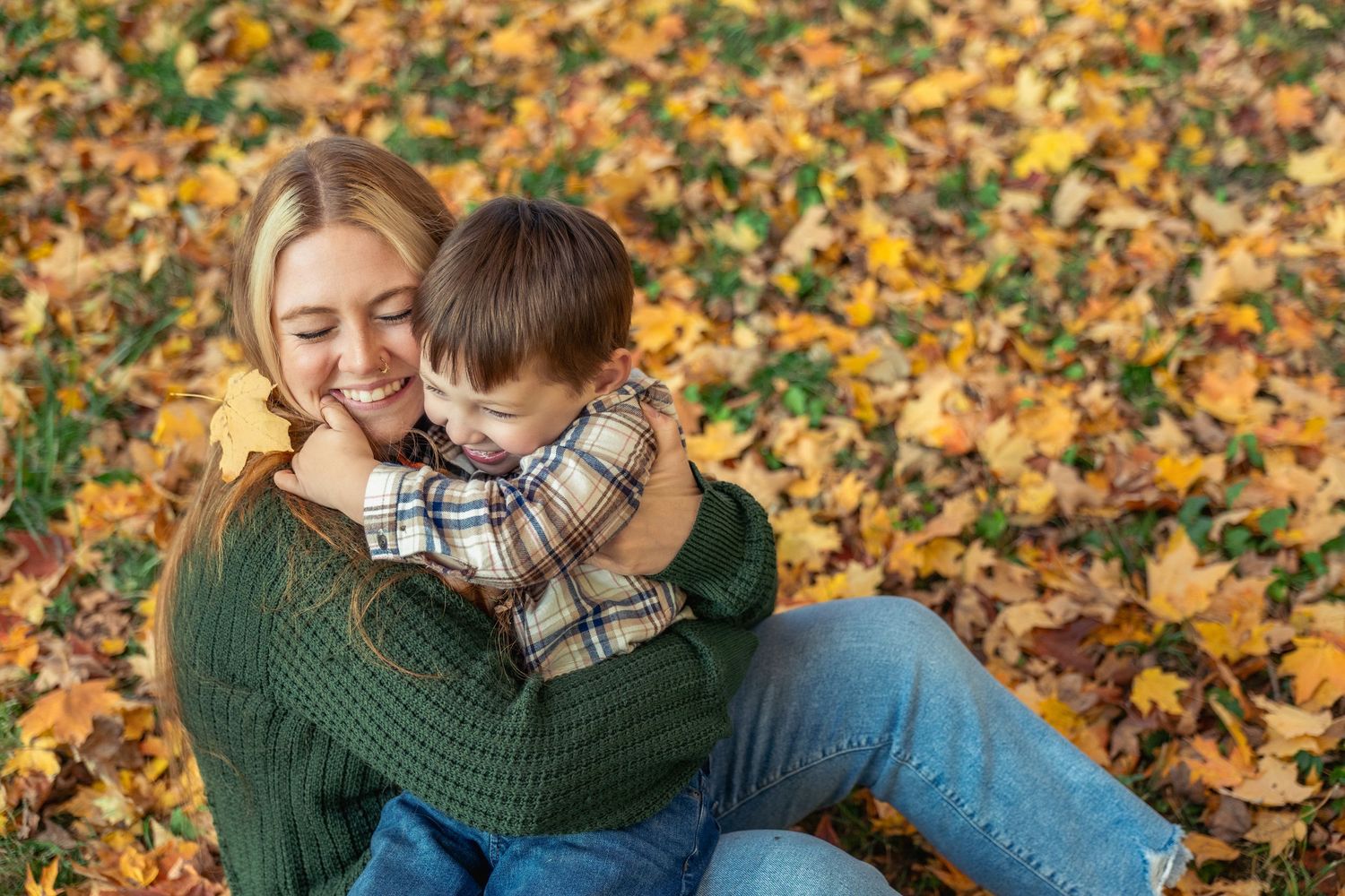 Autumn family photoshoot with colorful fallen leaves in the background.
