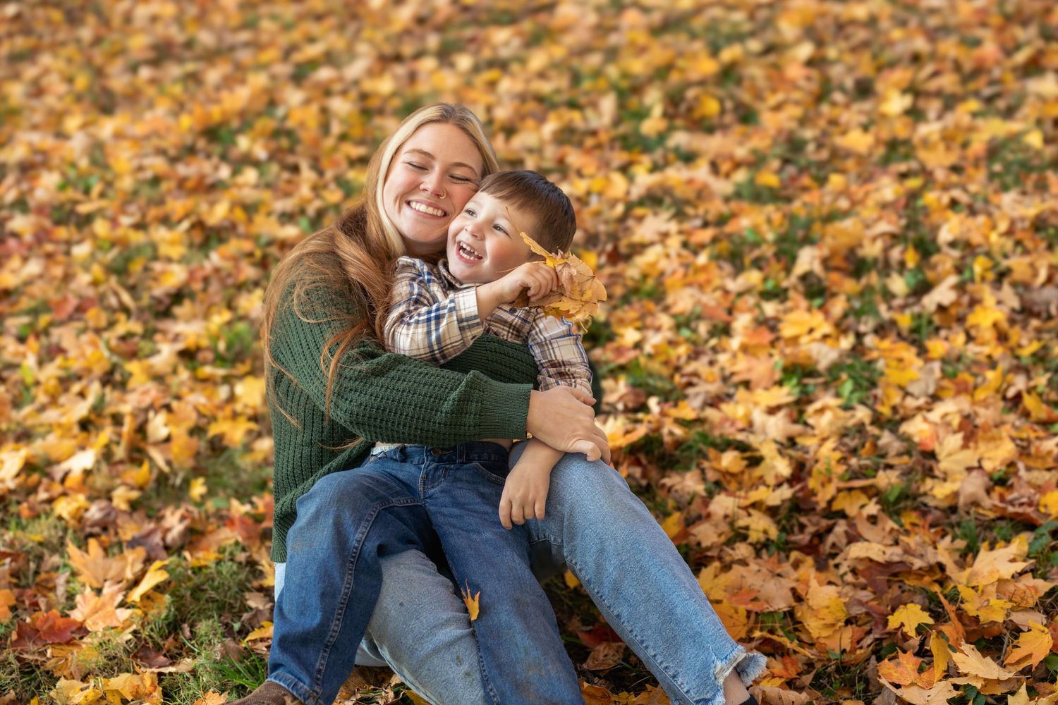 A couple sits together on fallen autumn leaves during a romantic outdoor photoshoot.