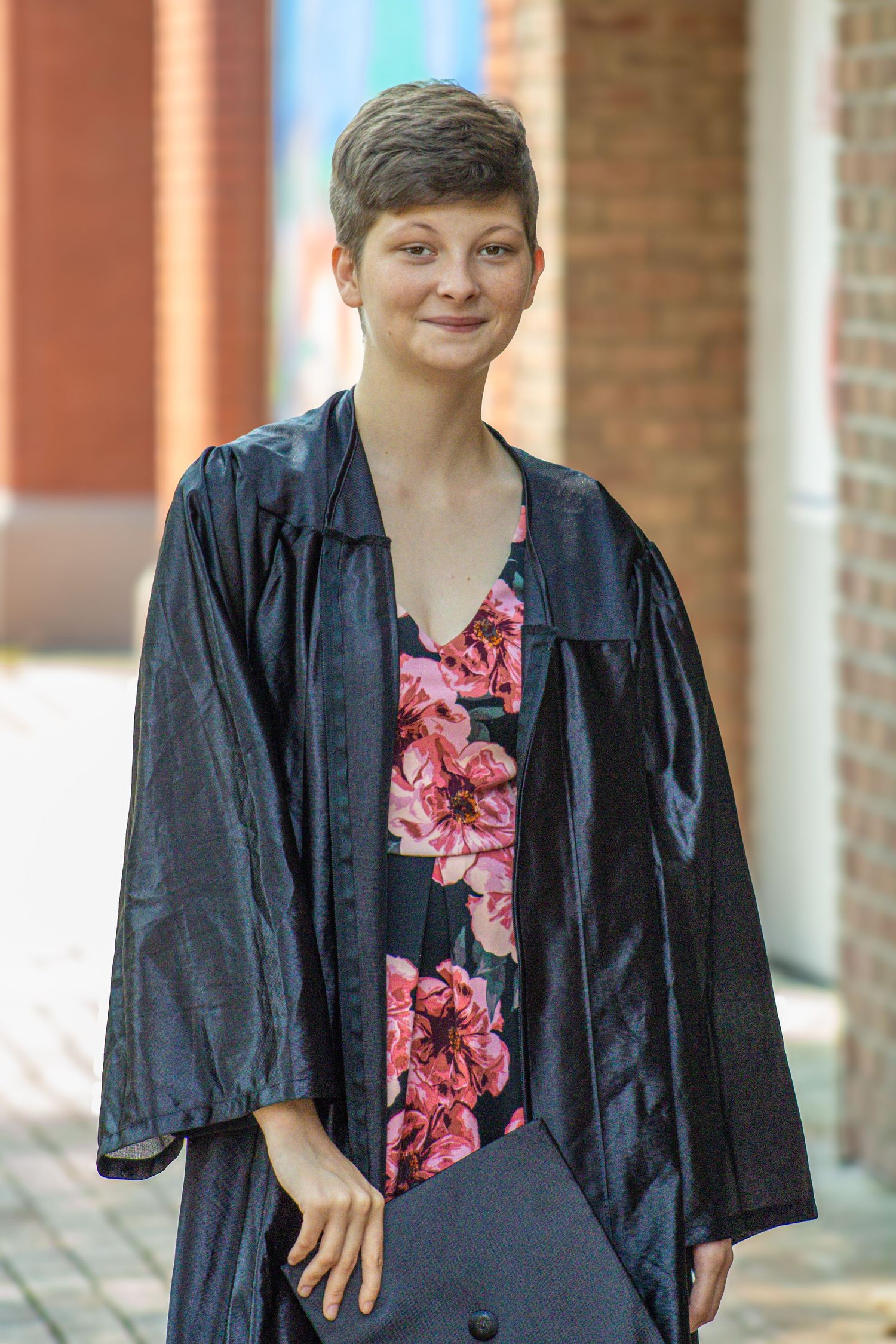 A person wearing a navy blazer over a pink floral top stands in front of a brick wall in a covered walkway.
