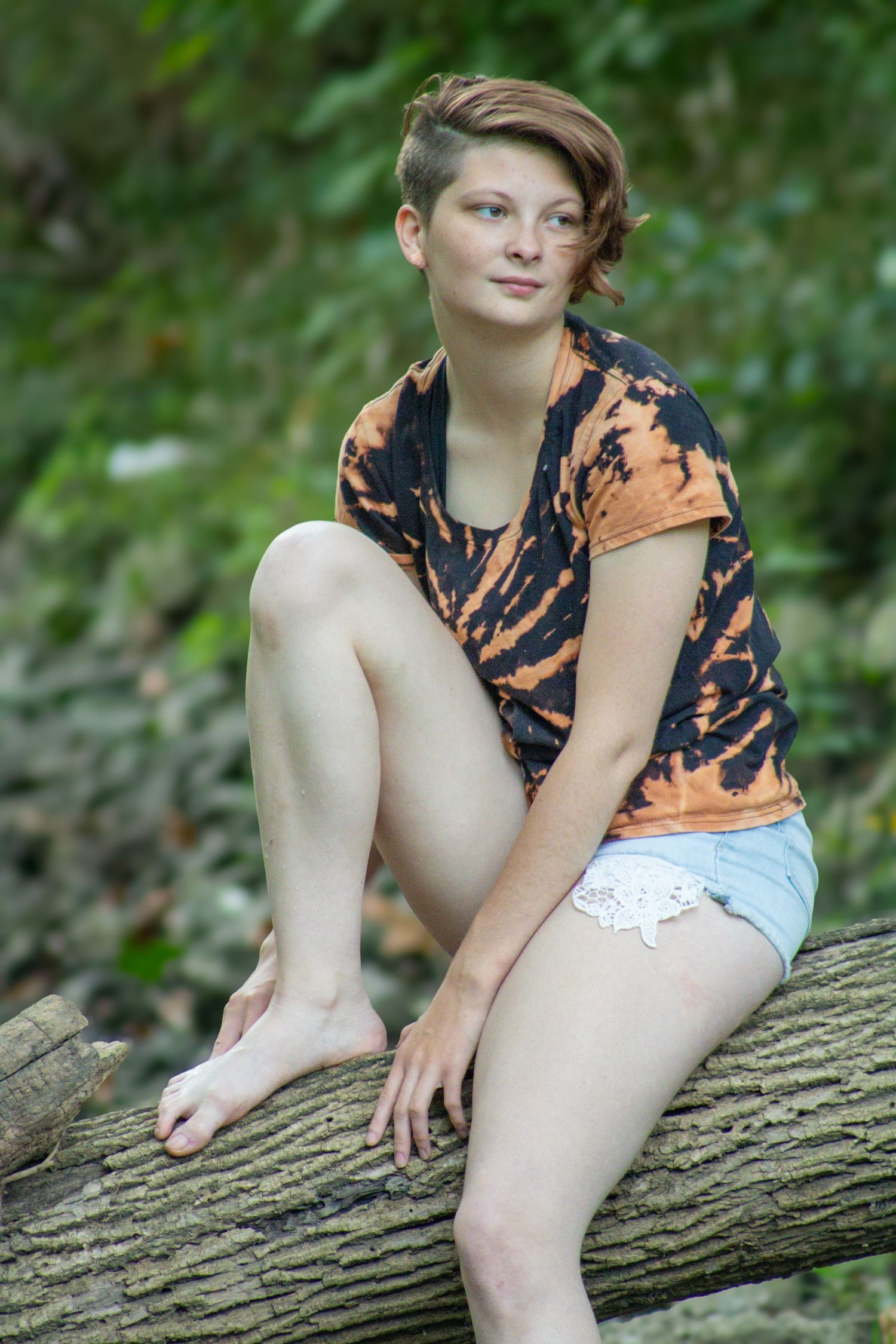 A person wearing orange tie-dye clothing sits on a fallen tree trunk in a natural outdoor setting.