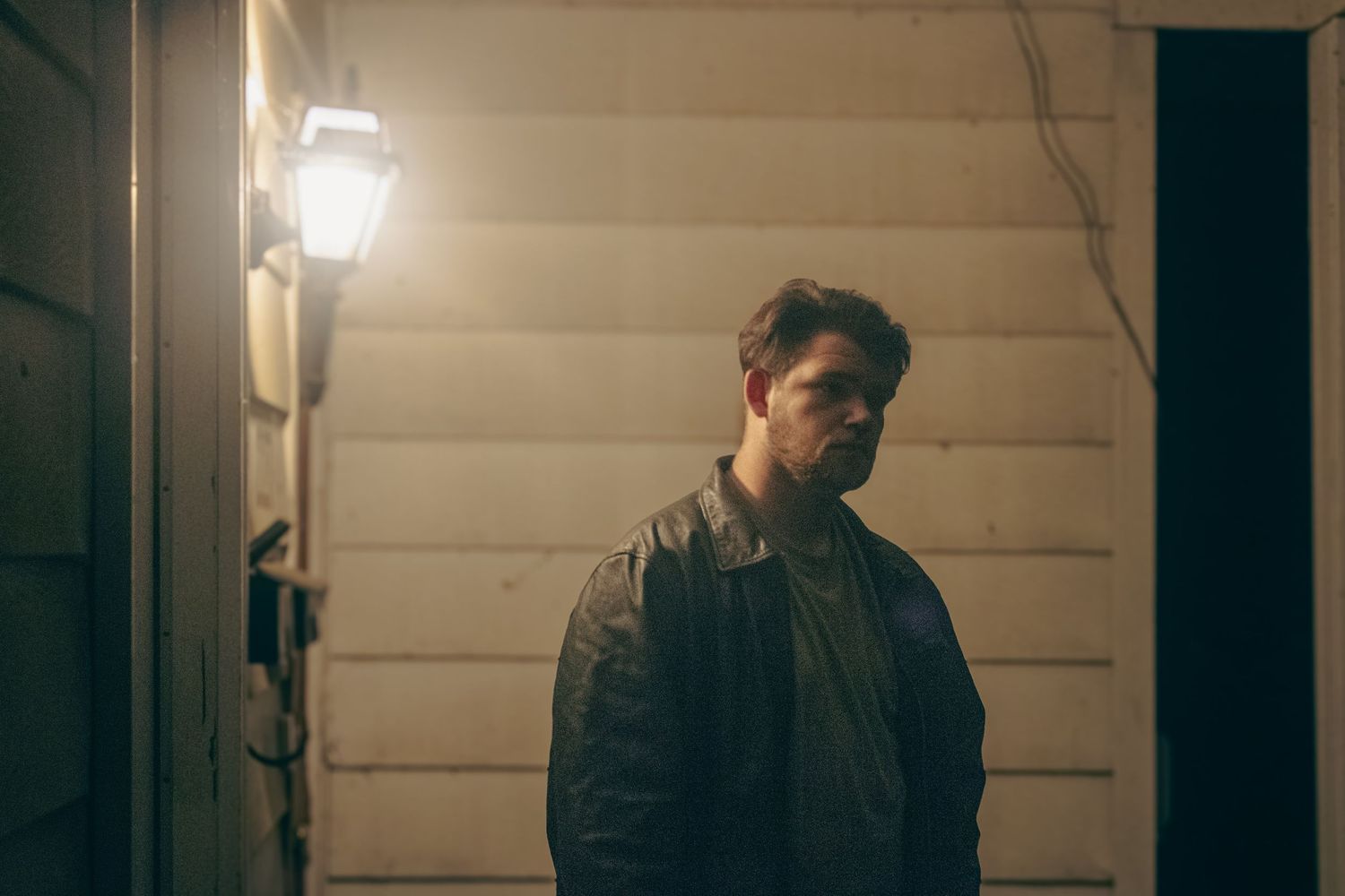 Person in a dark room stands against a wooden wall in dramatic lighting.
