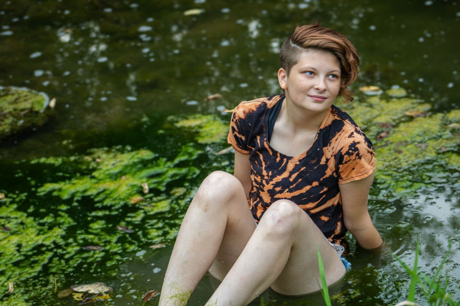 Person in a leopard print dress poses playfully by a tranquil pond surrounded by lush greenery.