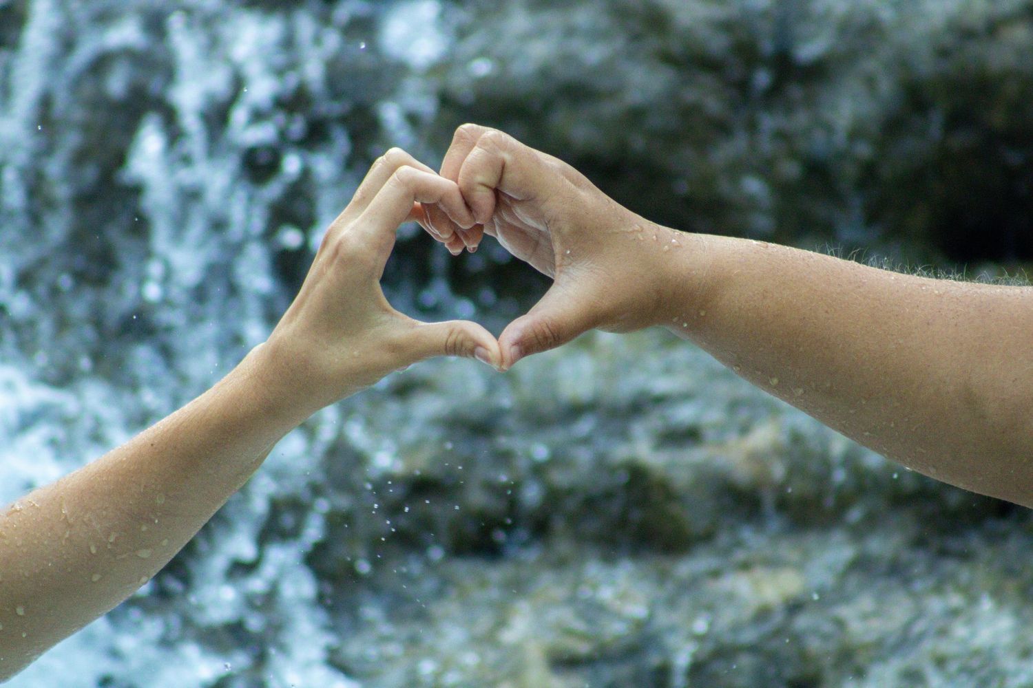 Two hands reach out to exchange a small white object against a blurred natural background.