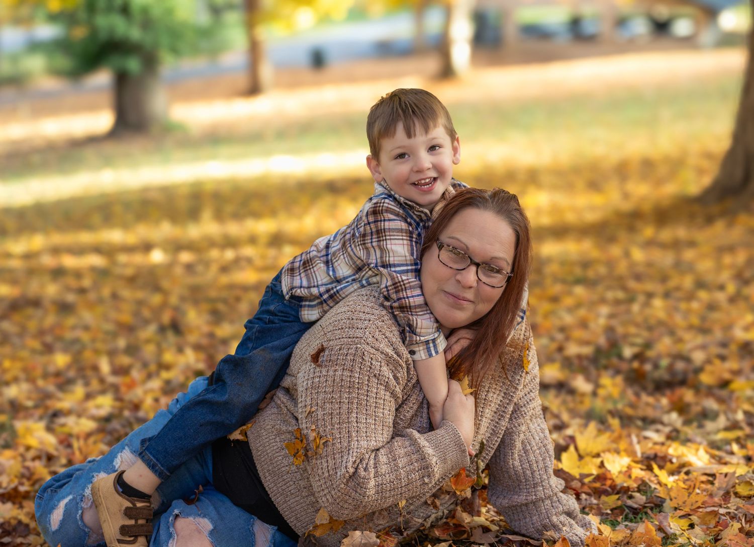 A playful autumn scene with people laying in fallen yellow leaves on a sunny day.