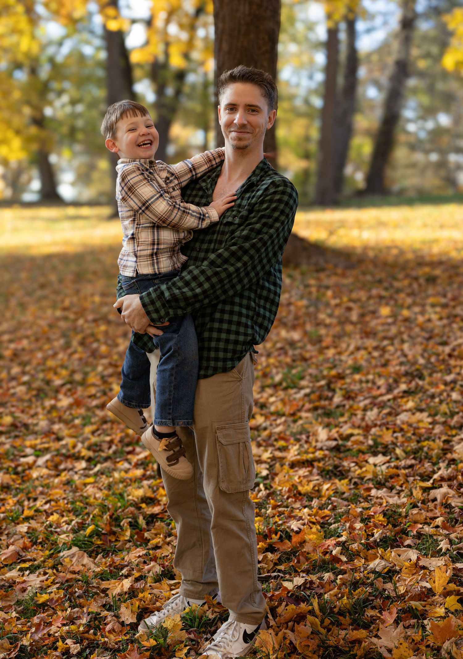 A parent and child play together in a park filled with golden autumn leaves on a sunny fall afternoon.