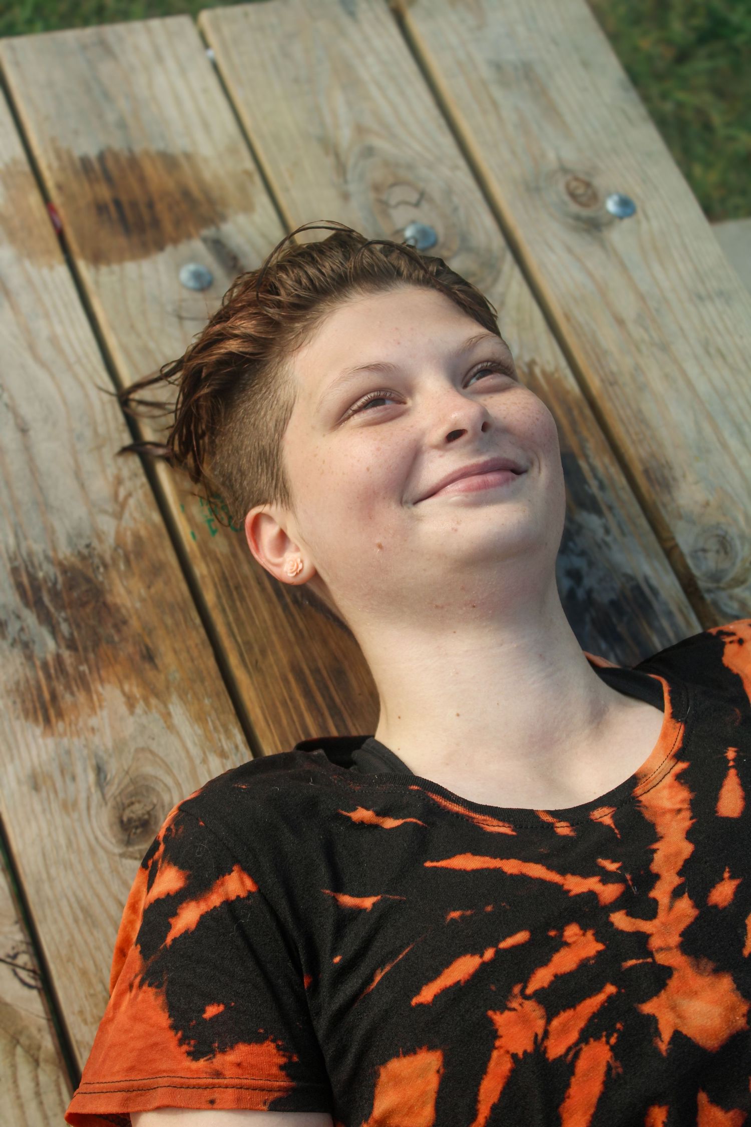 Person smiling while lying on wooden deck in bright sunlight.