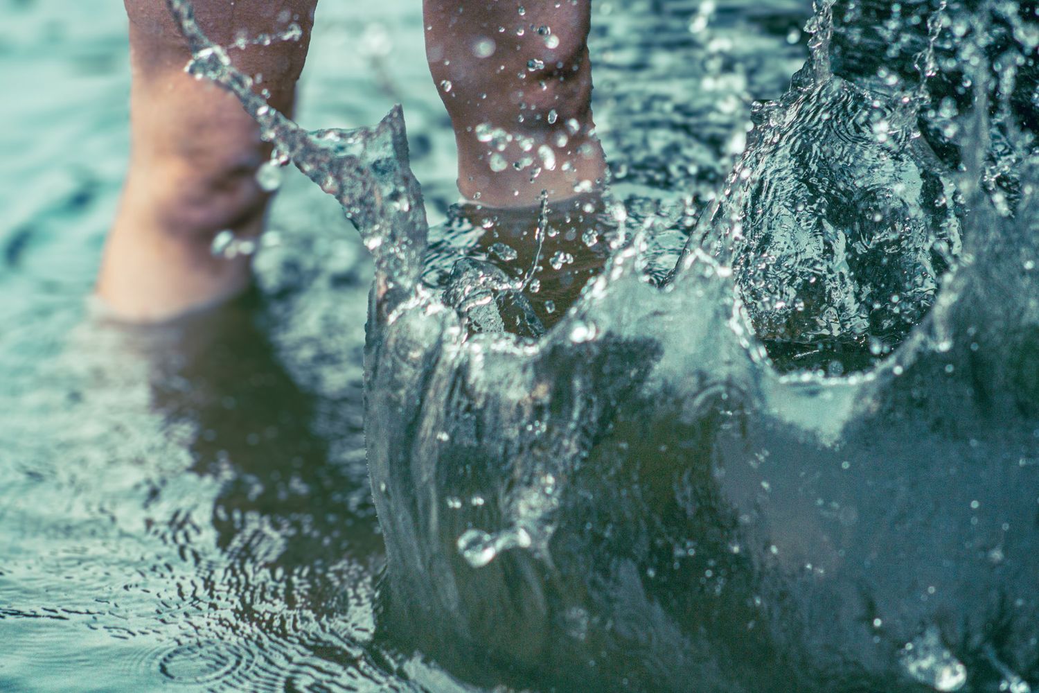 Close-up shot of feet splashing in turquoise water creating dynamic water droplets and ripples.