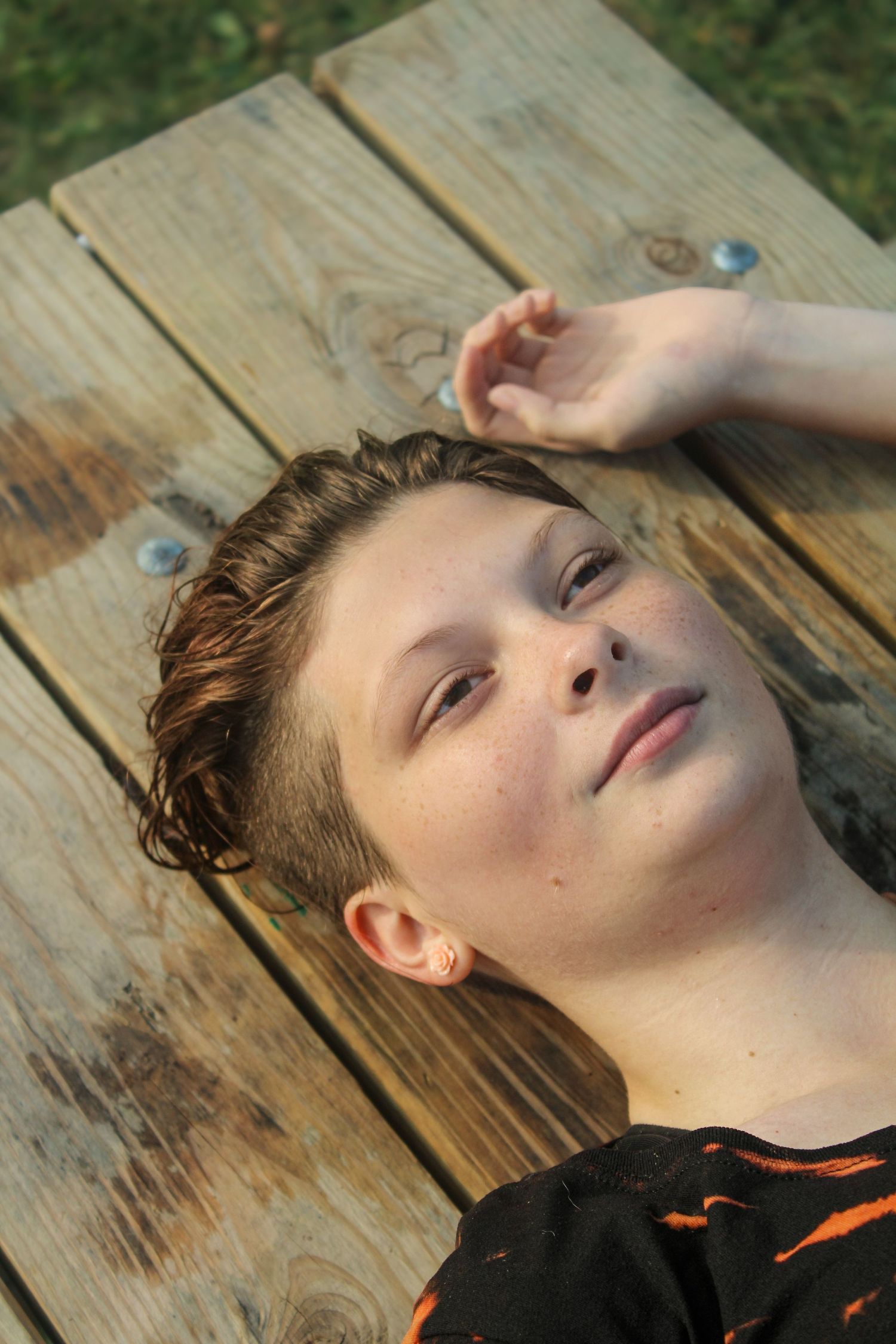A figure lying down on wooden deck boards with a relaxed expression in natural lighting.