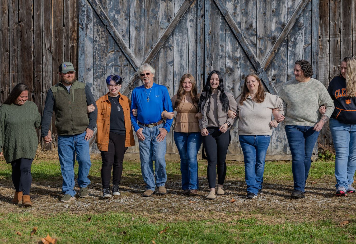 A group of people walking together in a line while holding hands in front of a rustic wooden barn wall.