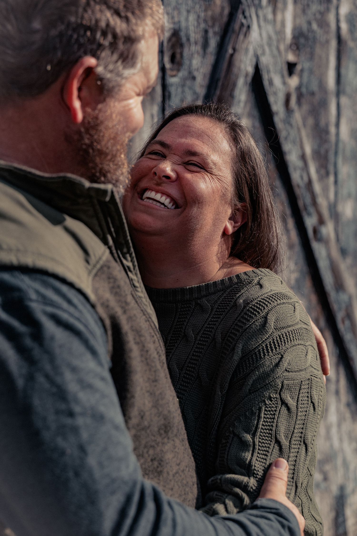 A couple shares a tender moment of laughter and joy while standing against a rocky cliff background.