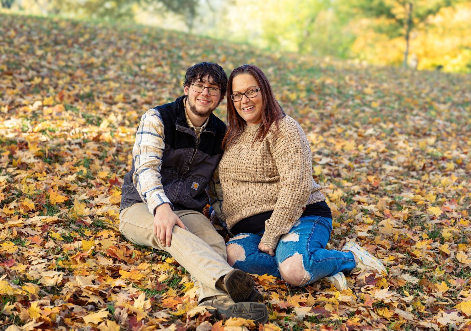 People sitting together on autumn leaves during a fall photoshoot in a park.