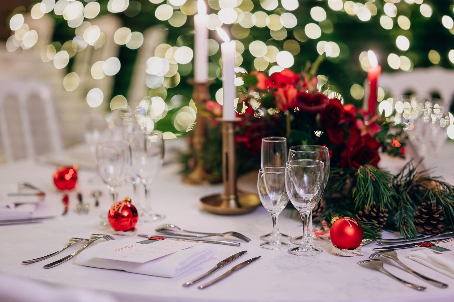 Elegant Christmas wedding reception table with white candles, red floral centerpiece, pine branches, and red ornaments.
