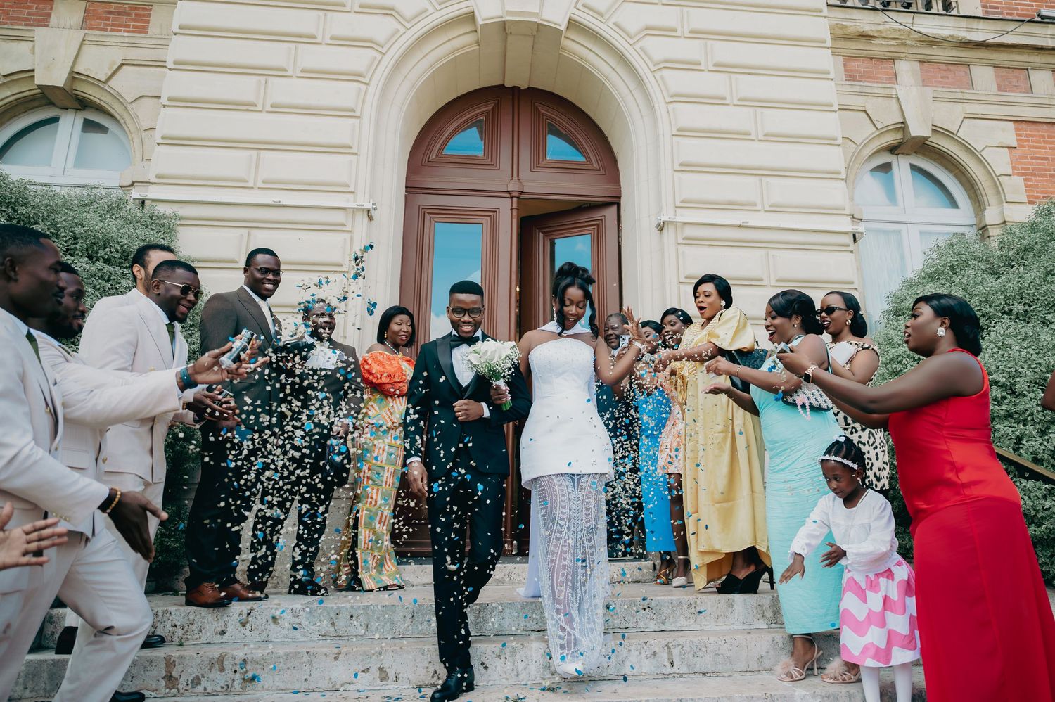 Joyful wedding party celebrating with confetti outside a historic stone building entrance.