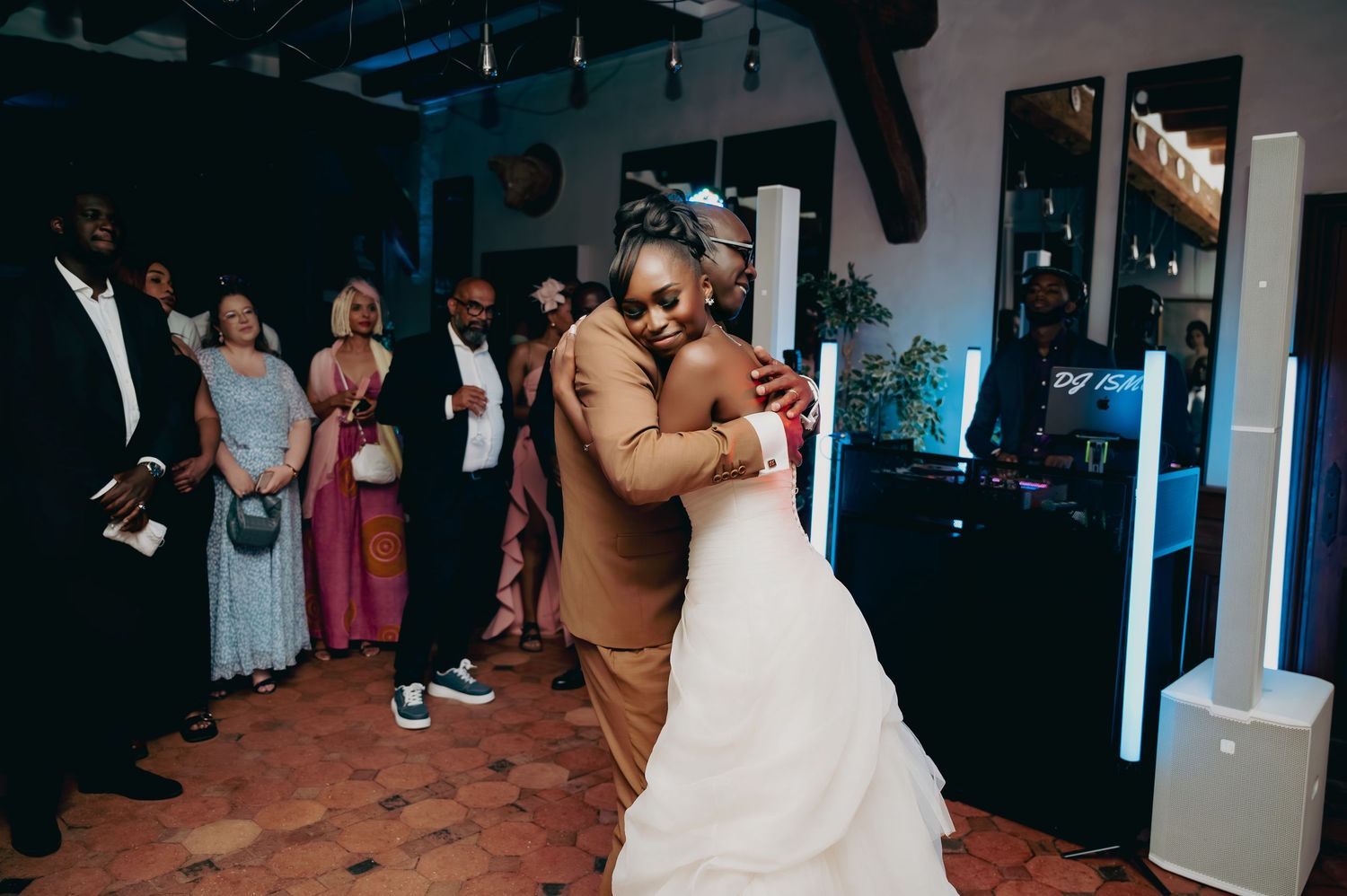 Bride and groom sharing their first dance at wedding reception while guests watch in elegant venue with blue lighting.
