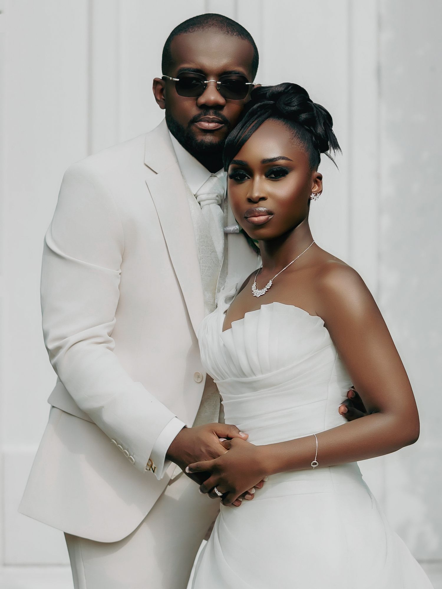 Elegant Black couple in coordinating ivory and white wedding attire pose for romantic portrait against white background.