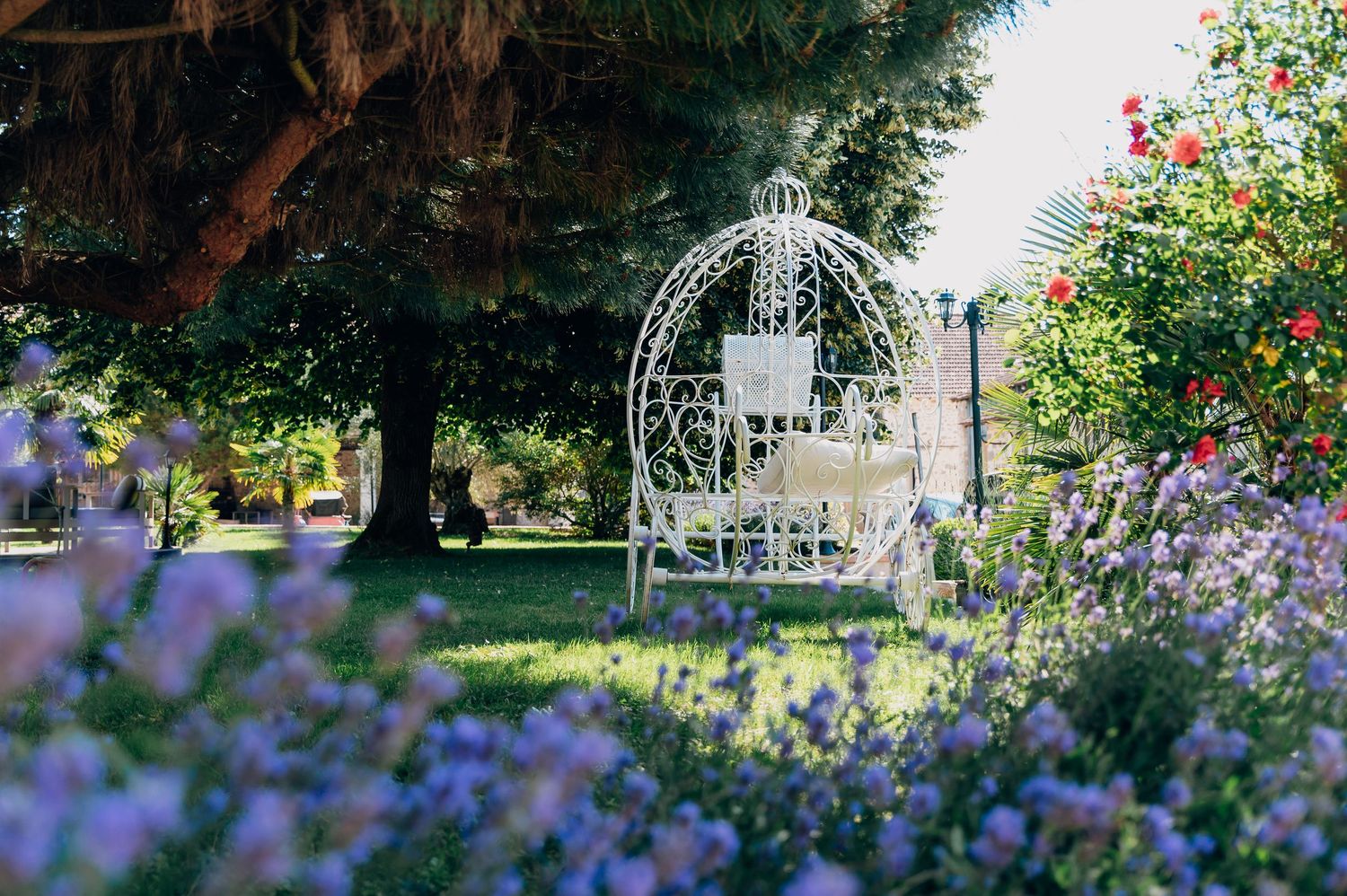 White ornate iron gazebo surrounded by purple lavender and colorful flowers in a romantic garden setting.