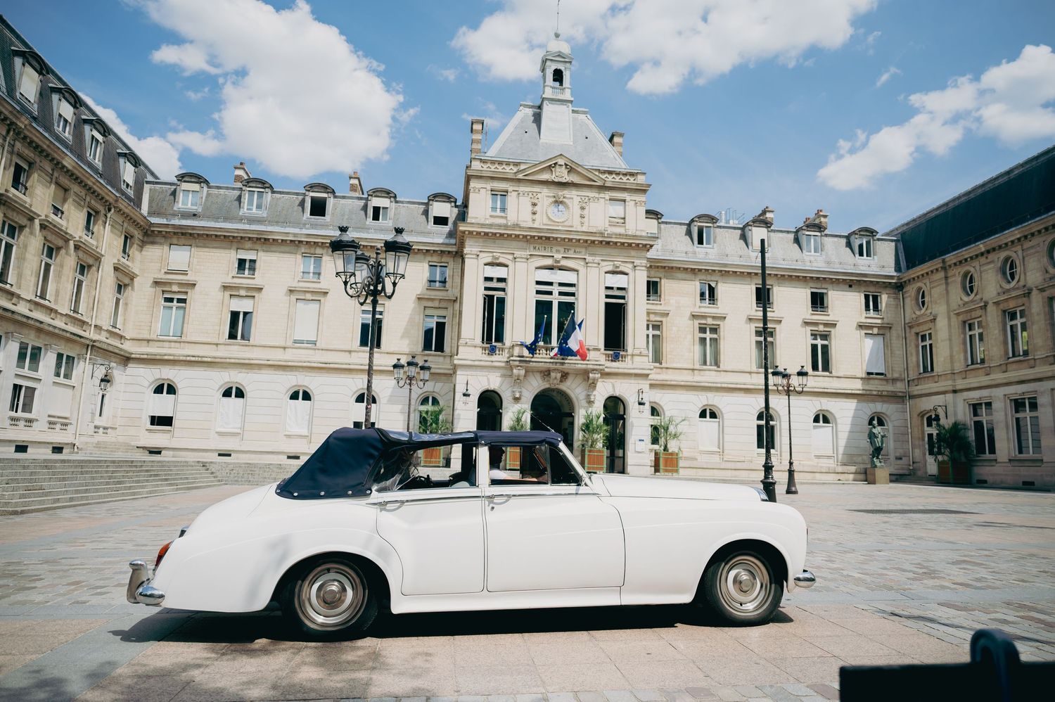Classic white vintage convertible car parked outside a grand French building on wedding day.