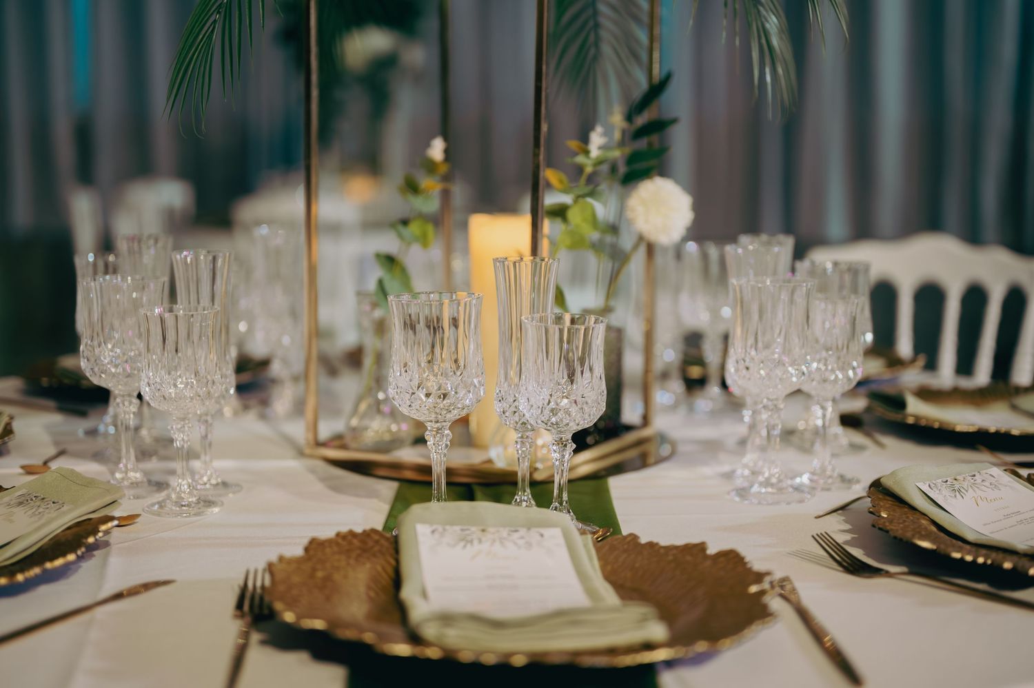 Elegant wedding reception table setting with crystal glassware, gold charger plates, and candles.