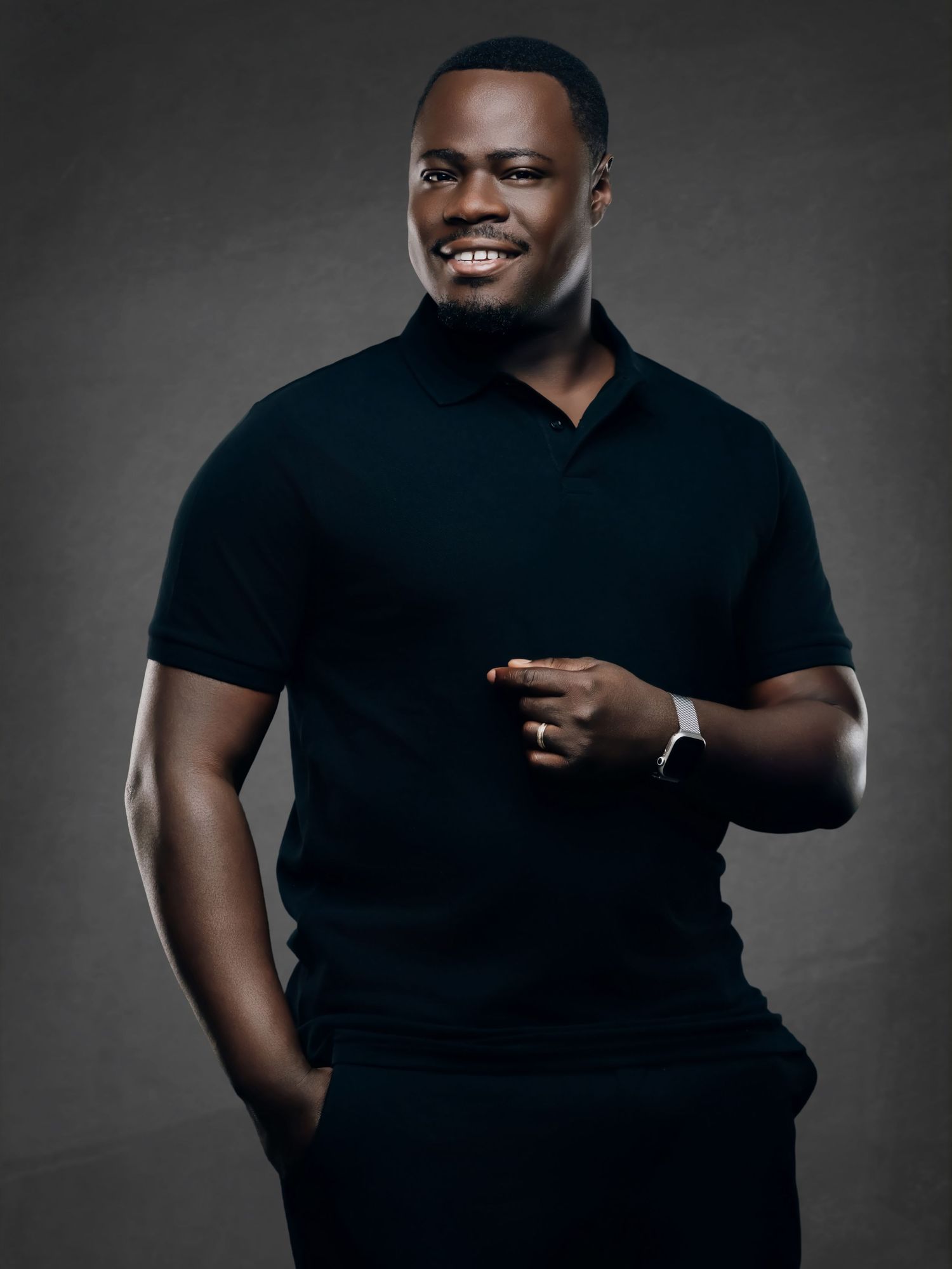 A cheerful Black man in a dark polo shirt smiles broadly in a professional studio portrait.
